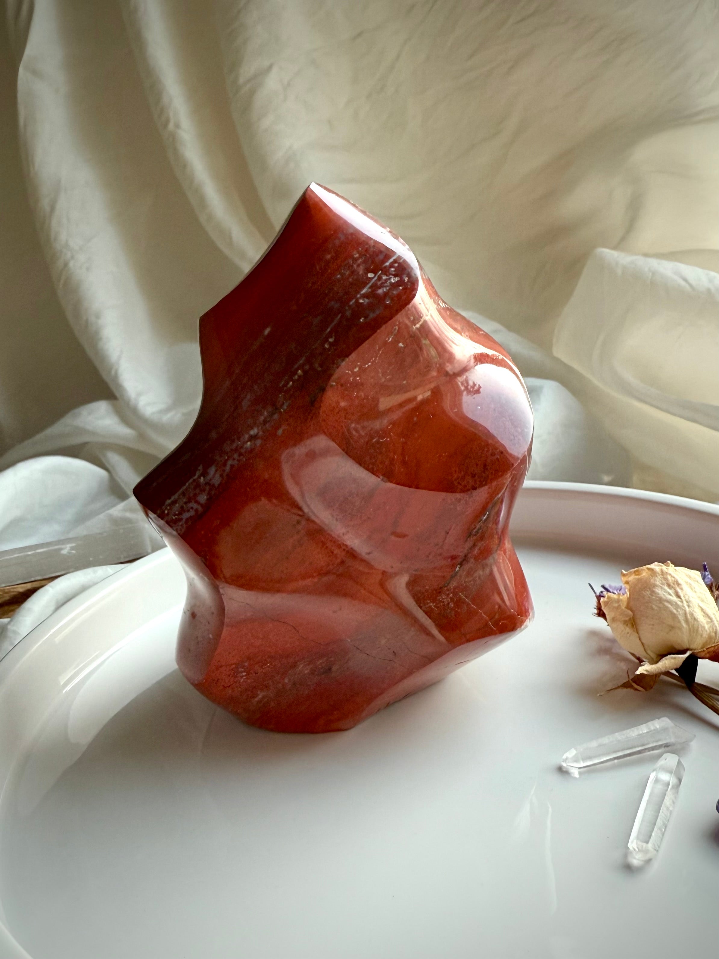 Red Ocean Jasper crystal flame displayed on a white tray with dried flowers and quartz points.