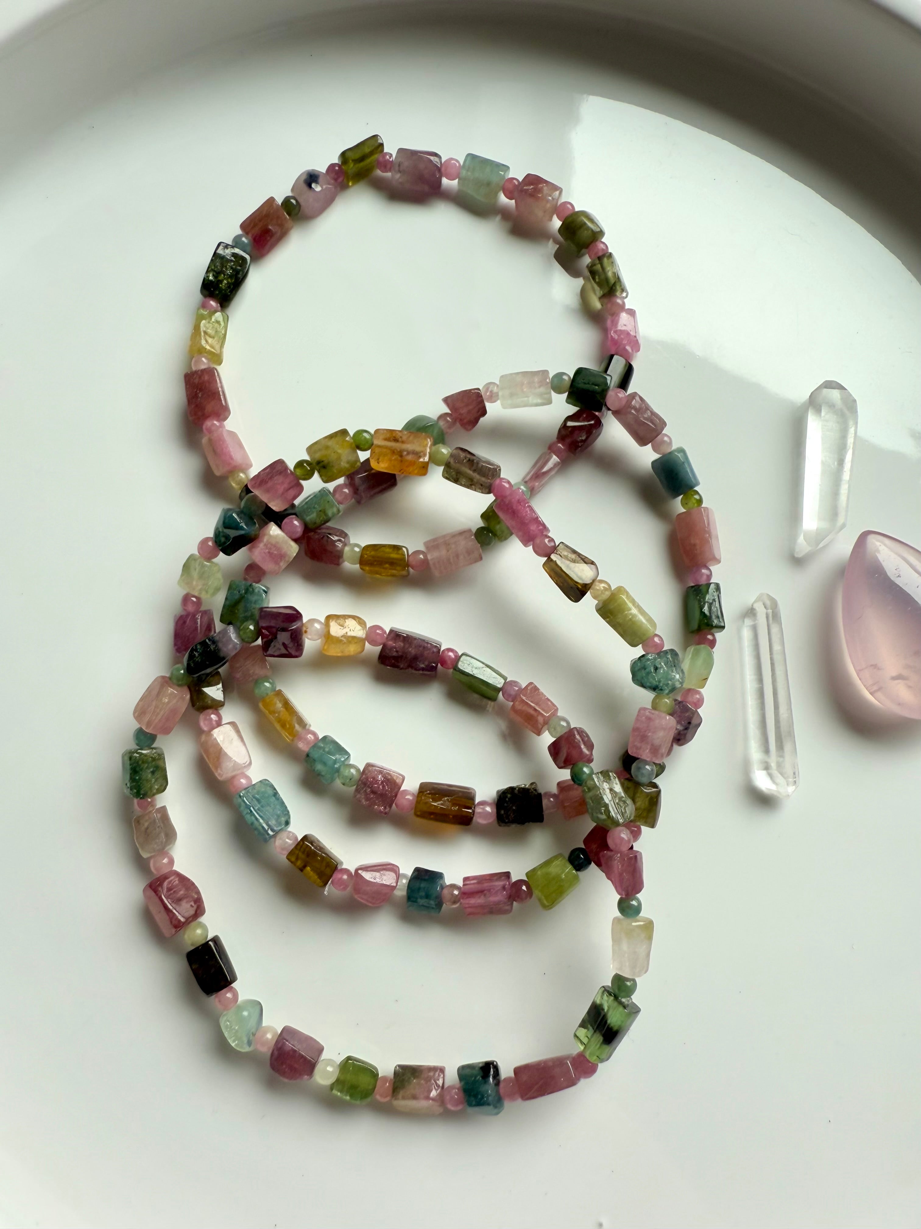 An array of Rainbow Tourmaline Bracelets made with irregular cube shaped gems shown on a white plate