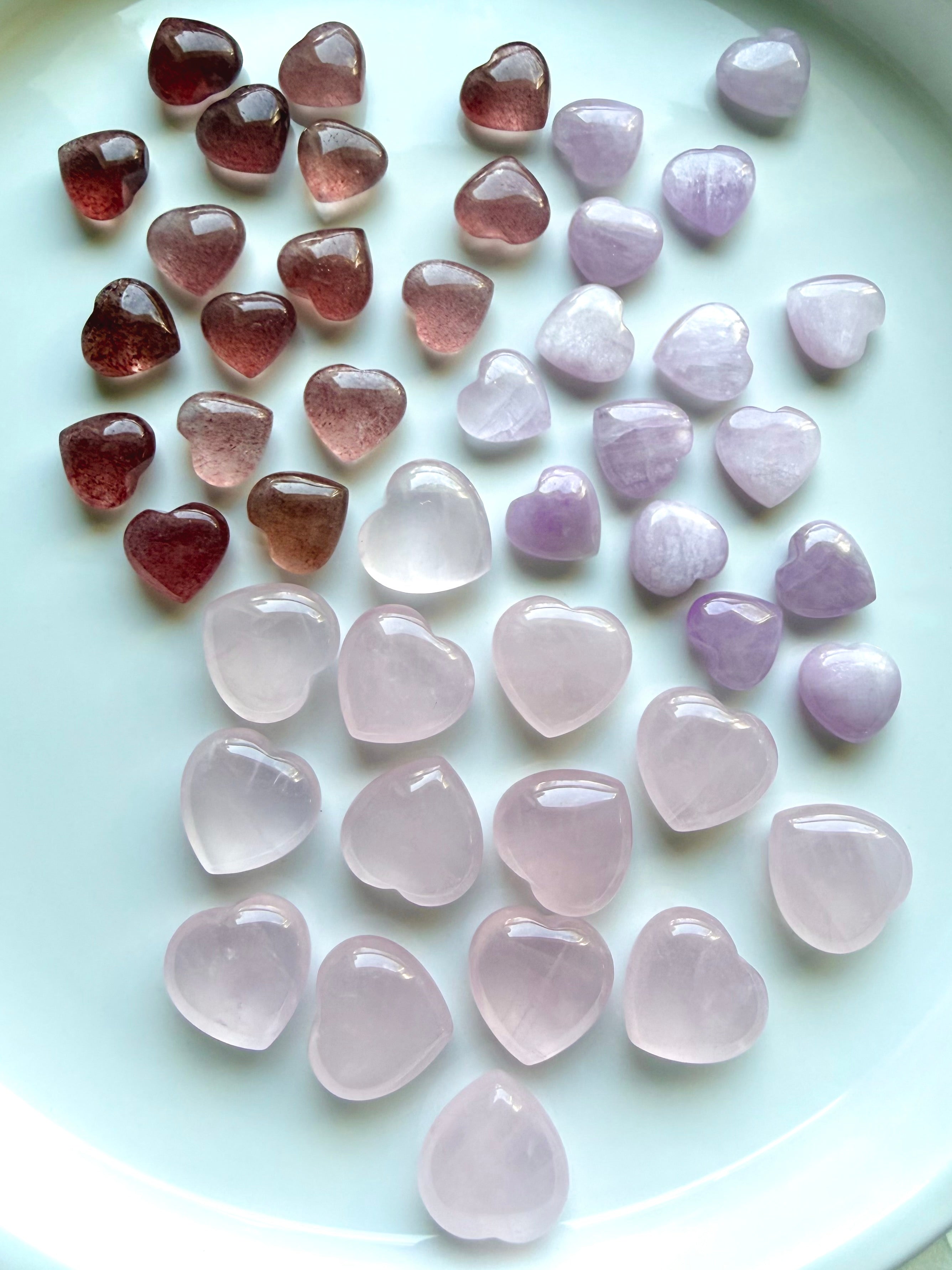 Mini rose quartz, strawberry quartz, and kunzite crystal hearts arranged together to show size, shape, and color differences