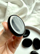 Polished Black Obsidian worry stone held in hand – thumb stone for anxiety relief, grounding + chakra healing