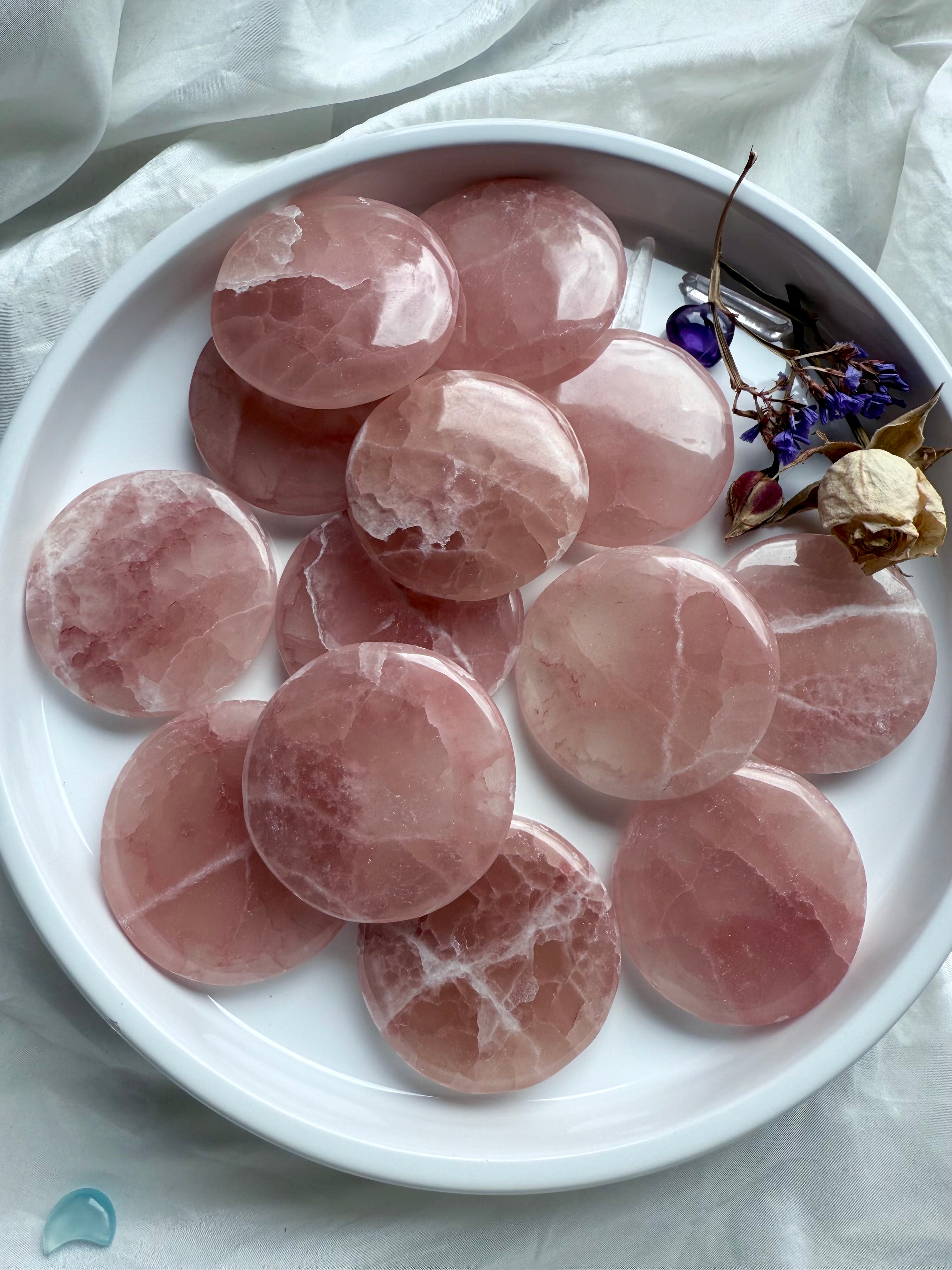 Rose Calcite meditation stones in soft pink hues displayed in a white dish with dried flowers and mini crystals – heart chakra crystal for love, peace, and emotional healing
