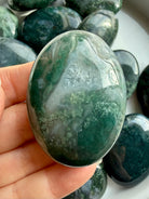 Hand holding moss agate palm stone showing natural dendritic patterns, soothing crystal for nervous system support