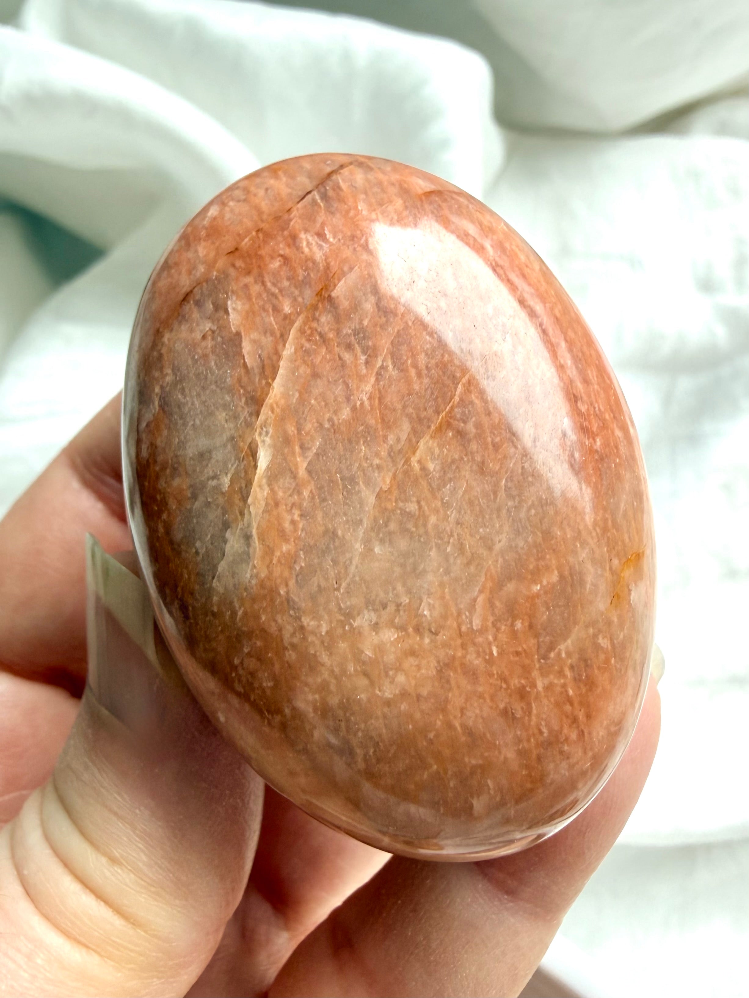 Large Peach Moonstone palm stone held in hand showing natural crack lines and warm orange peach hues