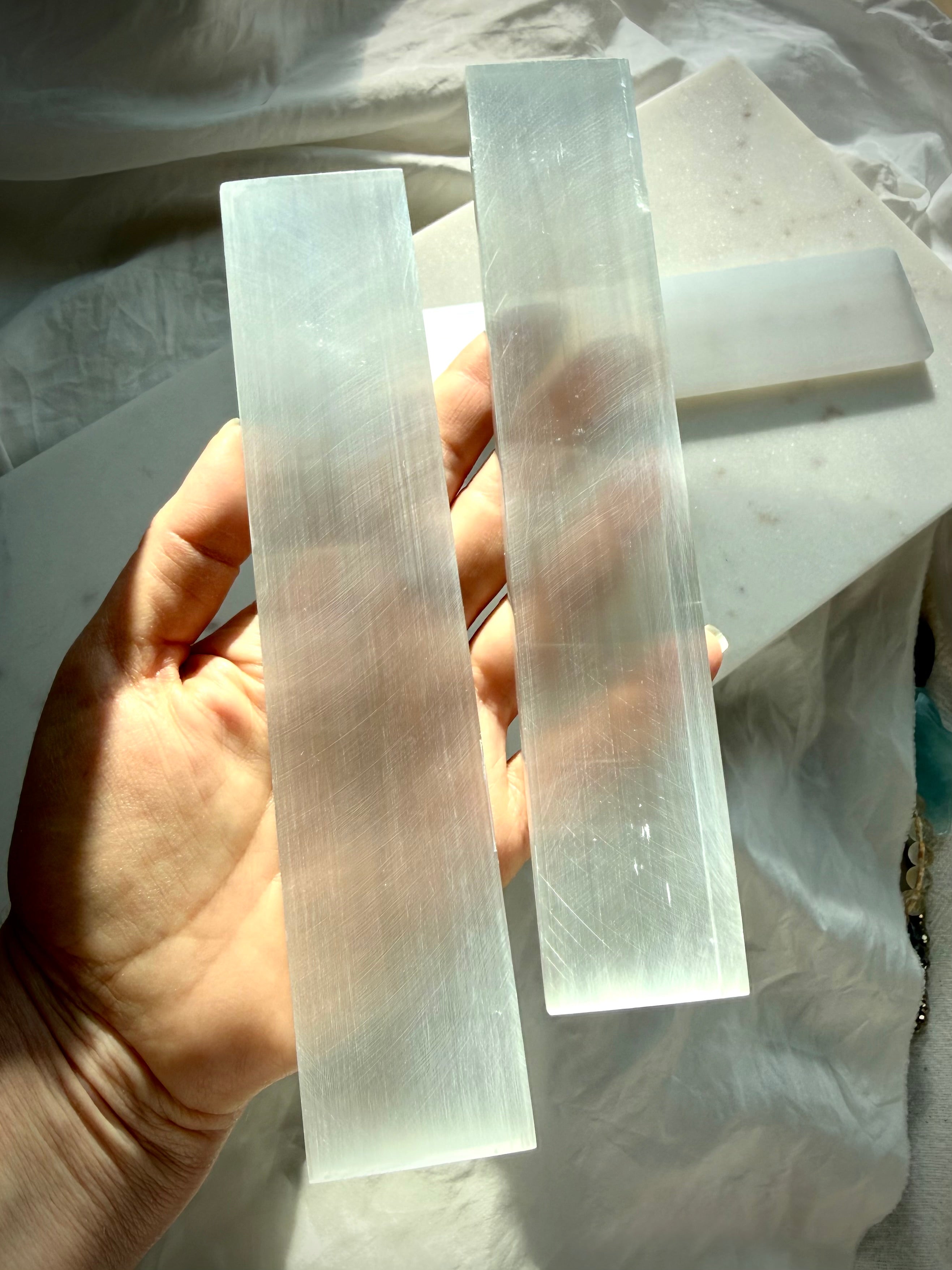 White Selenite charging bar held upright in sunlight, revealing natural Satin Spar striations and luminous crystal translucence