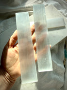 White Selenite charging bar held upright in sunlight, revealing natural Satin Spar striations and luminous crystal translucence