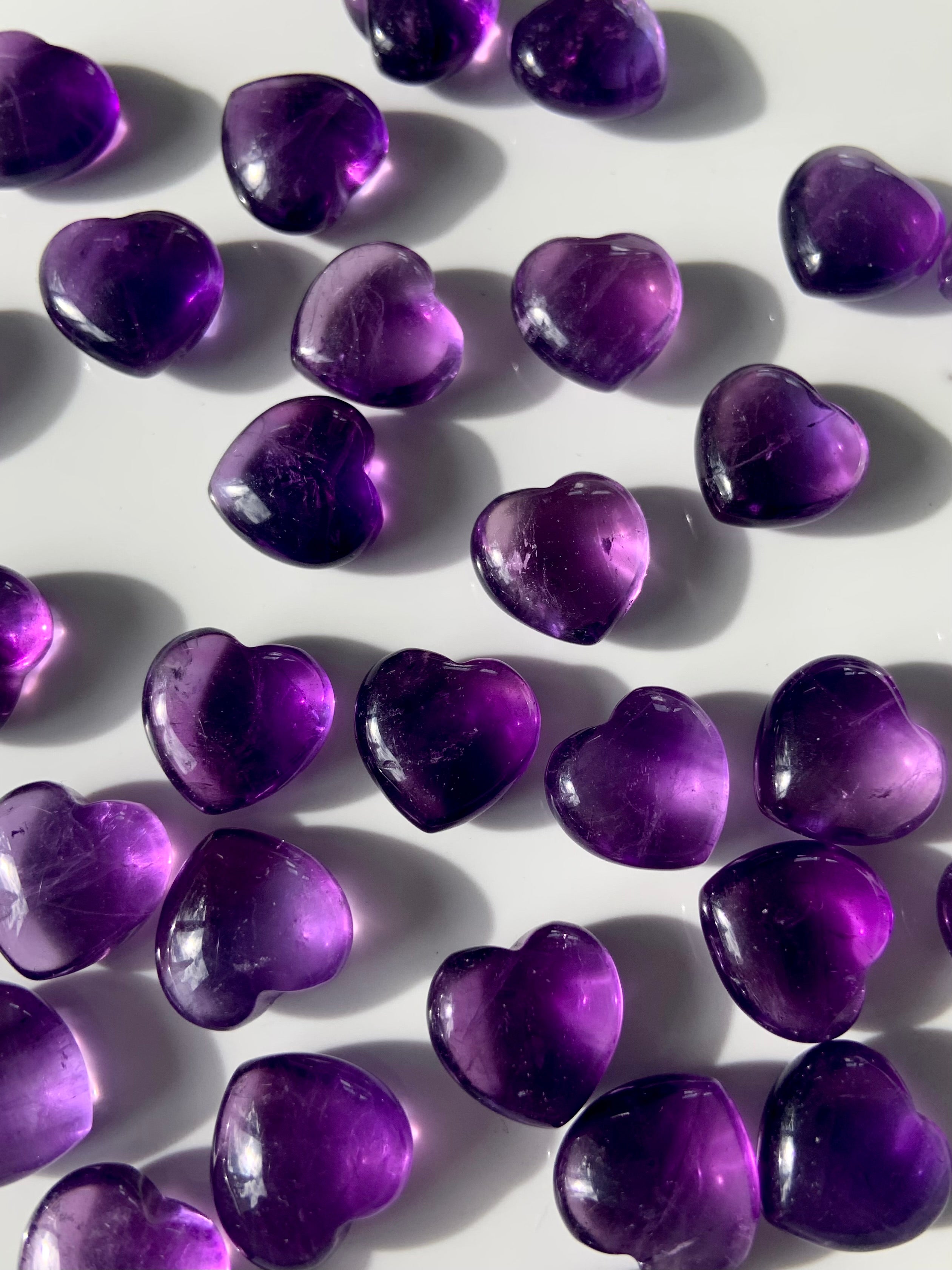 Array of gemmy purple Amethyst hearts on a white background — mini crystals for crown chakra healing