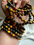 Hand holding several vibrant bumblebee jasper bracelets, vivid yellow-orange stone with earthy black inclusions for vitality and inner strength