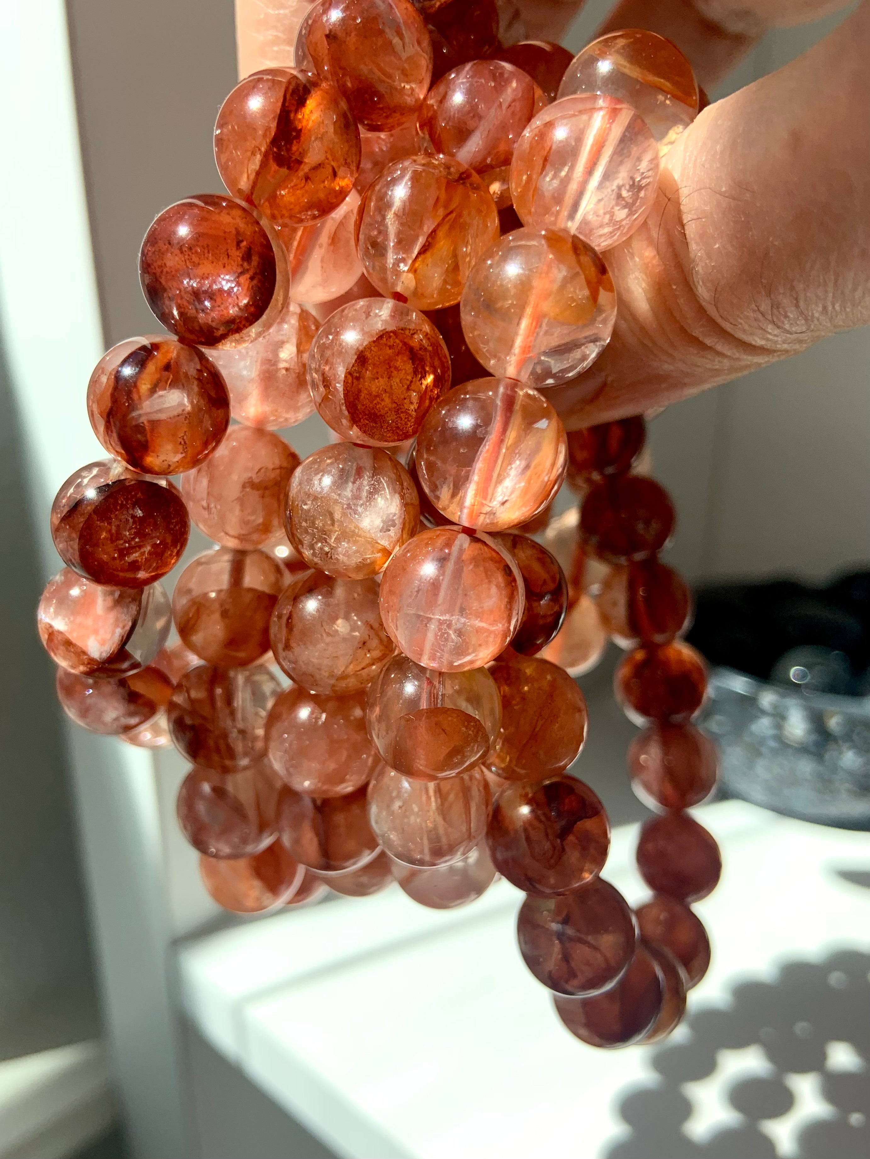Stack of Fire Quartz bracelets held to the light, highlighting the translucent beads and fiery inclusions of Hematoid Quartz