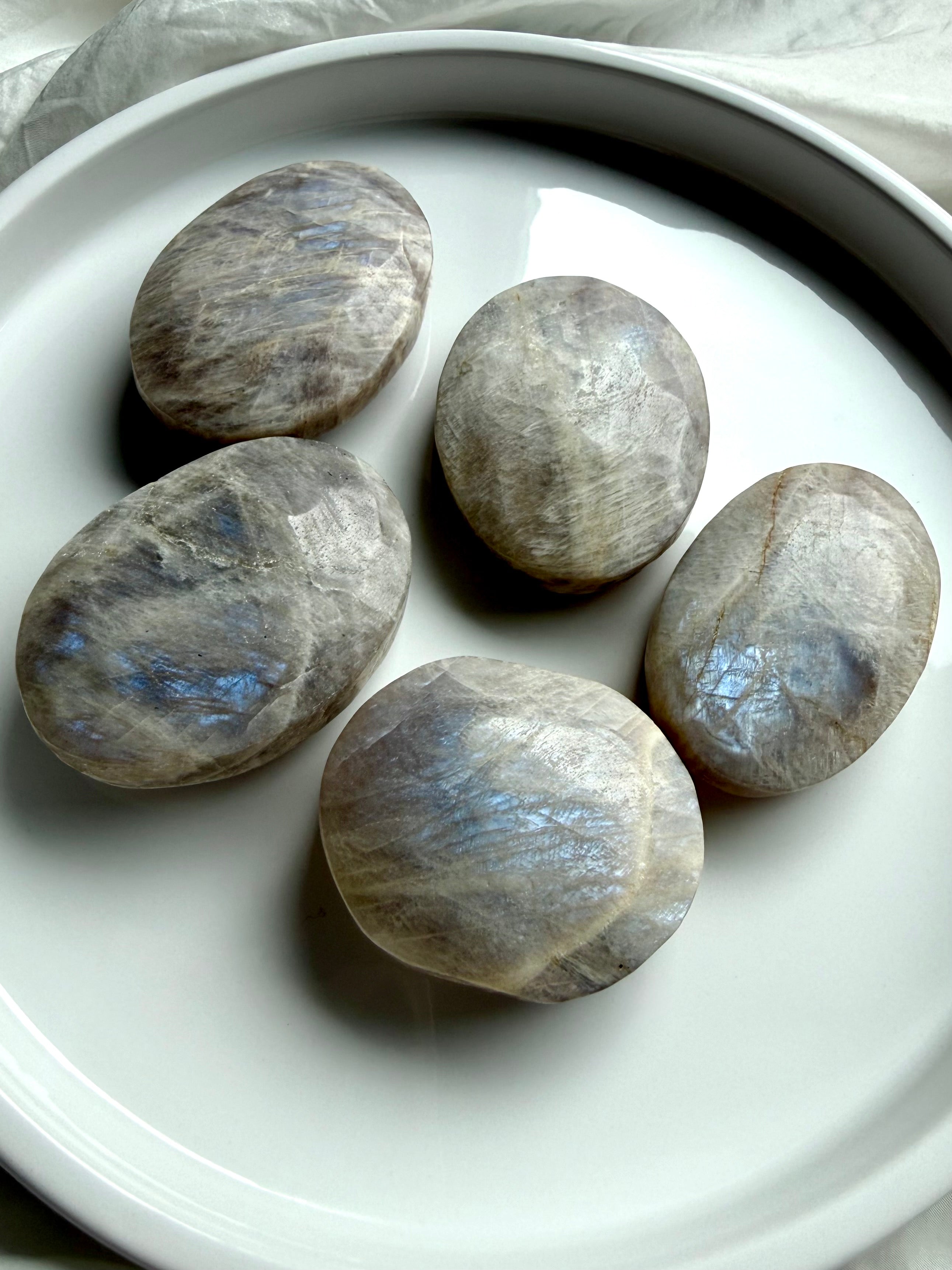 belomorite moonstone palm stones with blue flash and silvery shimmer on a white ceramic tray