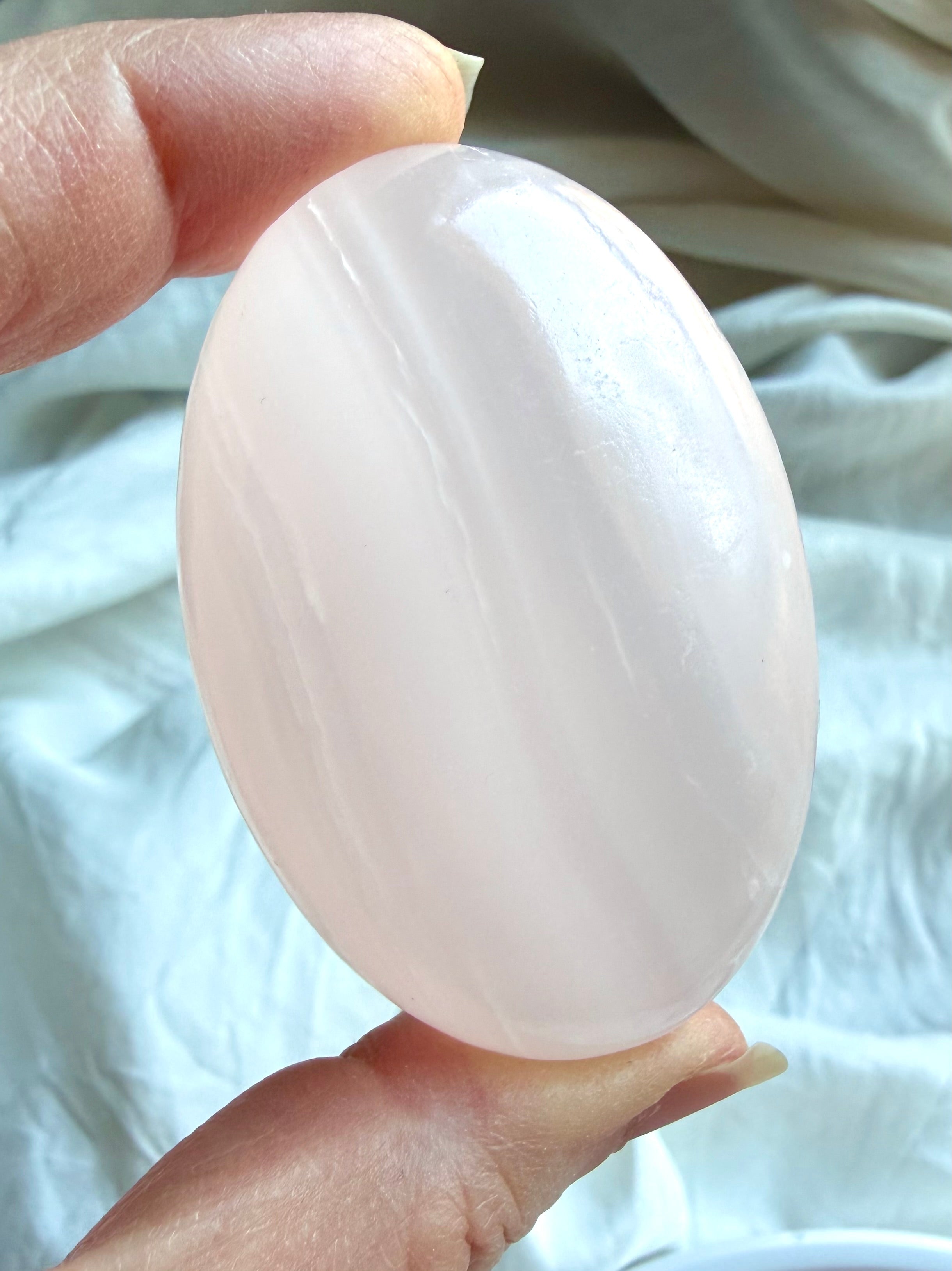Mangano Calcite palm stone held in hand with soft pink translucency and natural white banding