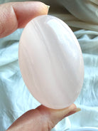 Mangano Calcite palm stone held in hand with soft pink translucency and natural white banding