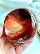 Hand holding a polished Red Carnelian crystal bowl with glowing orange and deep red banding – a sacred offering dish for Sacral Chakra healing rituals.