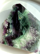 Flatlay of green and purple fluorite slab showing rainbow internal flashes and white scolecite snowflake inclusions
