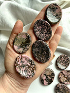 Rhodonite worry stones in hand showing pink and black spiderweb matrix patterns