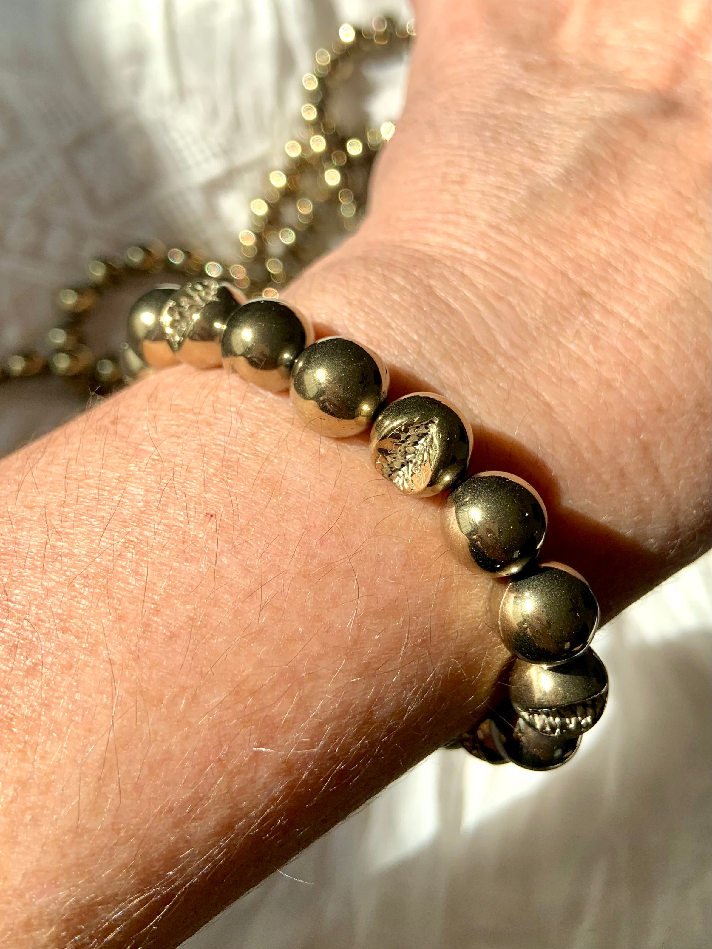 Pyrite beaded bracelet worn on wrist, reflecting light with metallic golden tones — healing crystal jewelry for strength & empowerment.