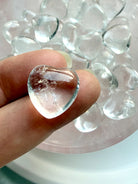 Mini Clear Quartz heart crystal on fingertip showing high clarity quartz with bowl of hearts in background