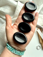 Black Obsidian palm stones lined up in hand – root chakra crystals for grounding, calming + daily energy clearing