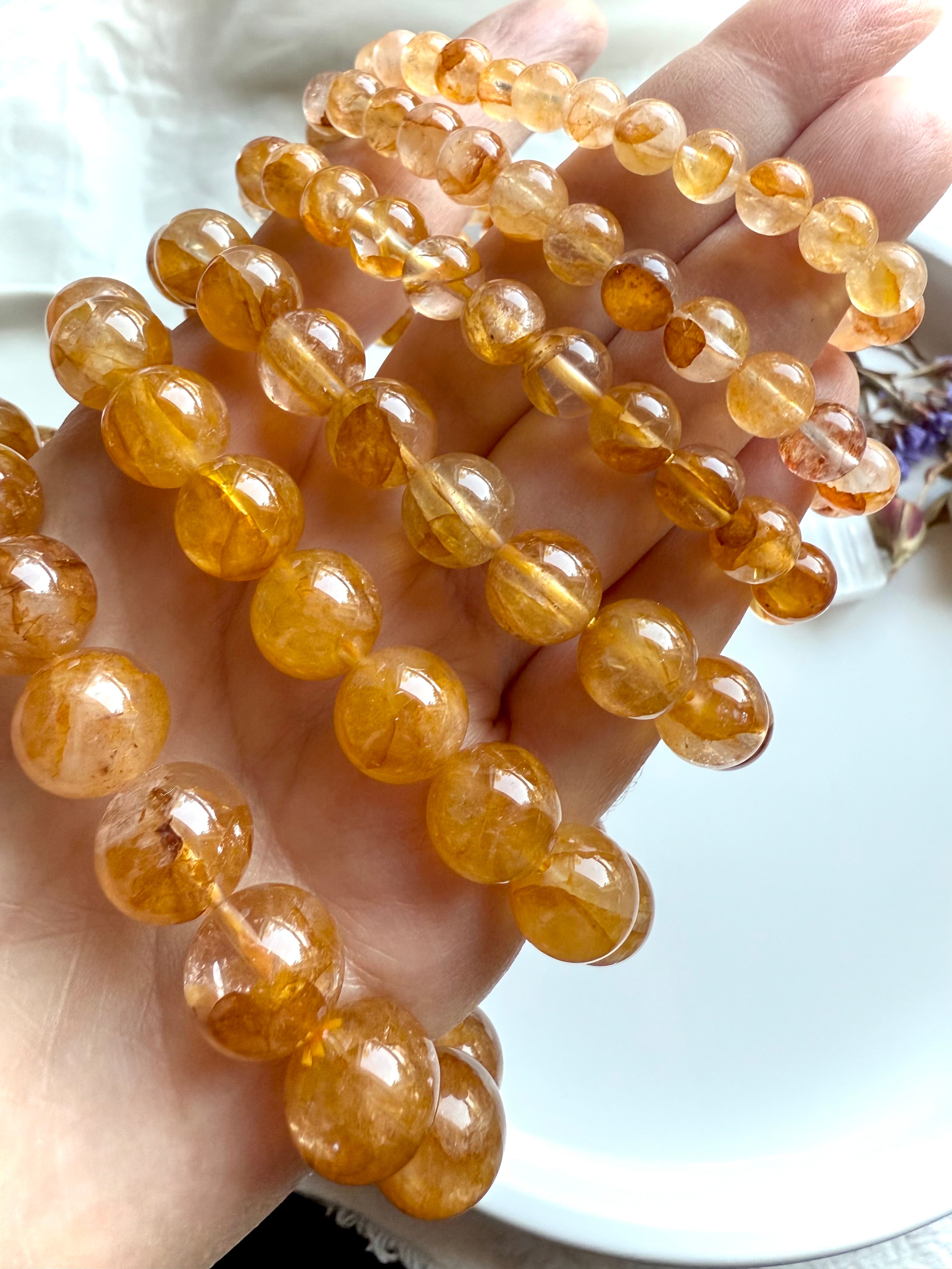 Angled view of stacked Golden Healer Quartz bracelets in bead sizes large to small, displayed on hand to highlight radiant color and inclusions.