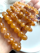 Angled view of stacked Golden Healer Quartz bracelets in bead sizes large to small, displayed on hand to highlight radiant color and inclusions.