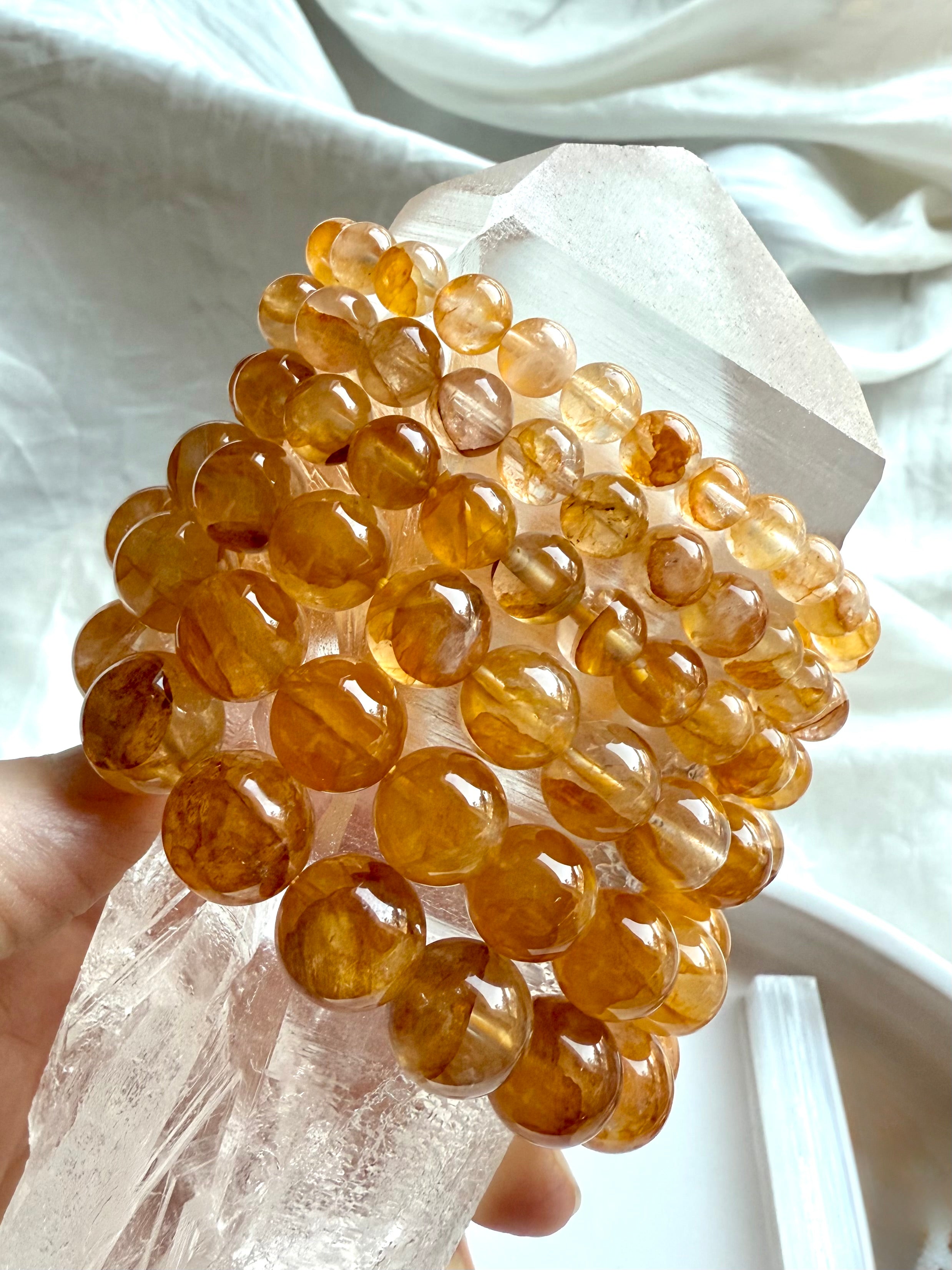 Stack of six high quality Golden Healer Quartz bracelets displayed on a large quartz point, showing bead sizes from large to small with luminous golden color and clarity.