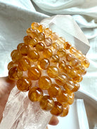 Stack of six high quality Golden Healer Quartz bracelets displayed on a large quartz point, showing bead sizes from large to small with luminous golden color and clarity.