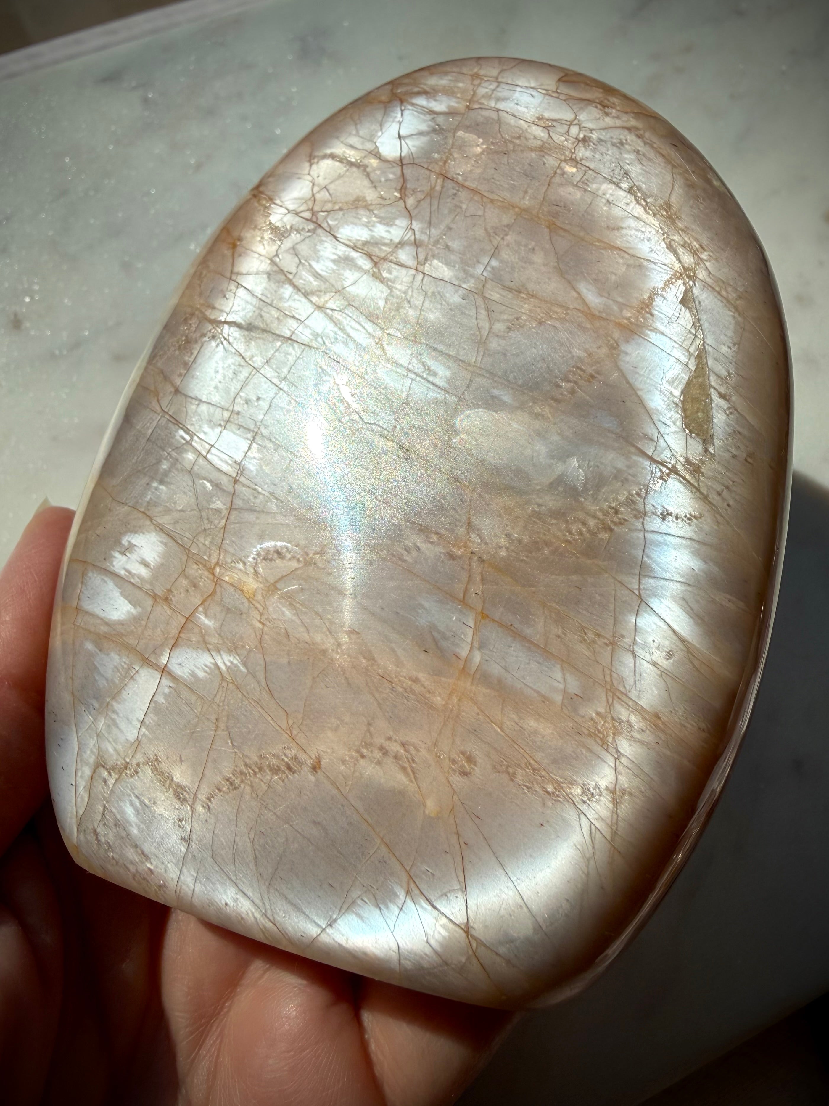 Peach Moonstone crystal freeform held in hand showing bright silver flash across the polished surface
