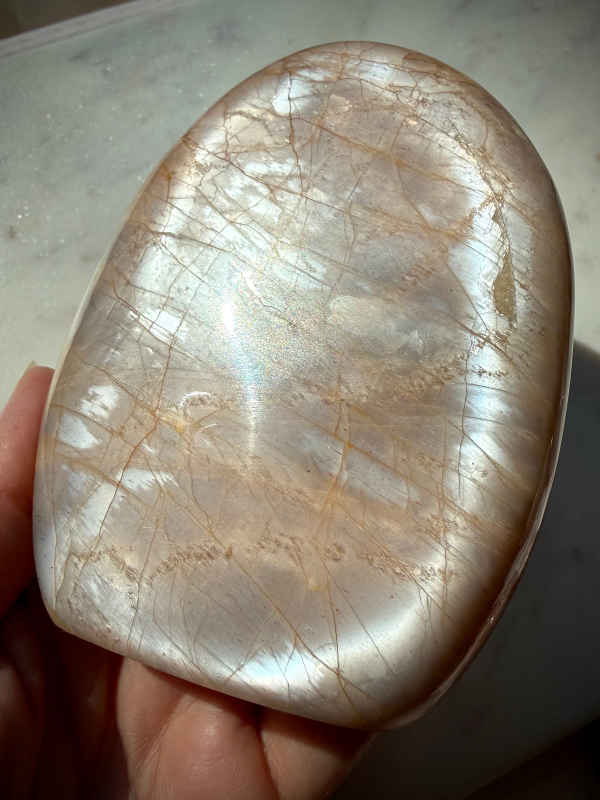 Peach Moonstone crystal freeform held in hand showing bright silver flash across the polished surface