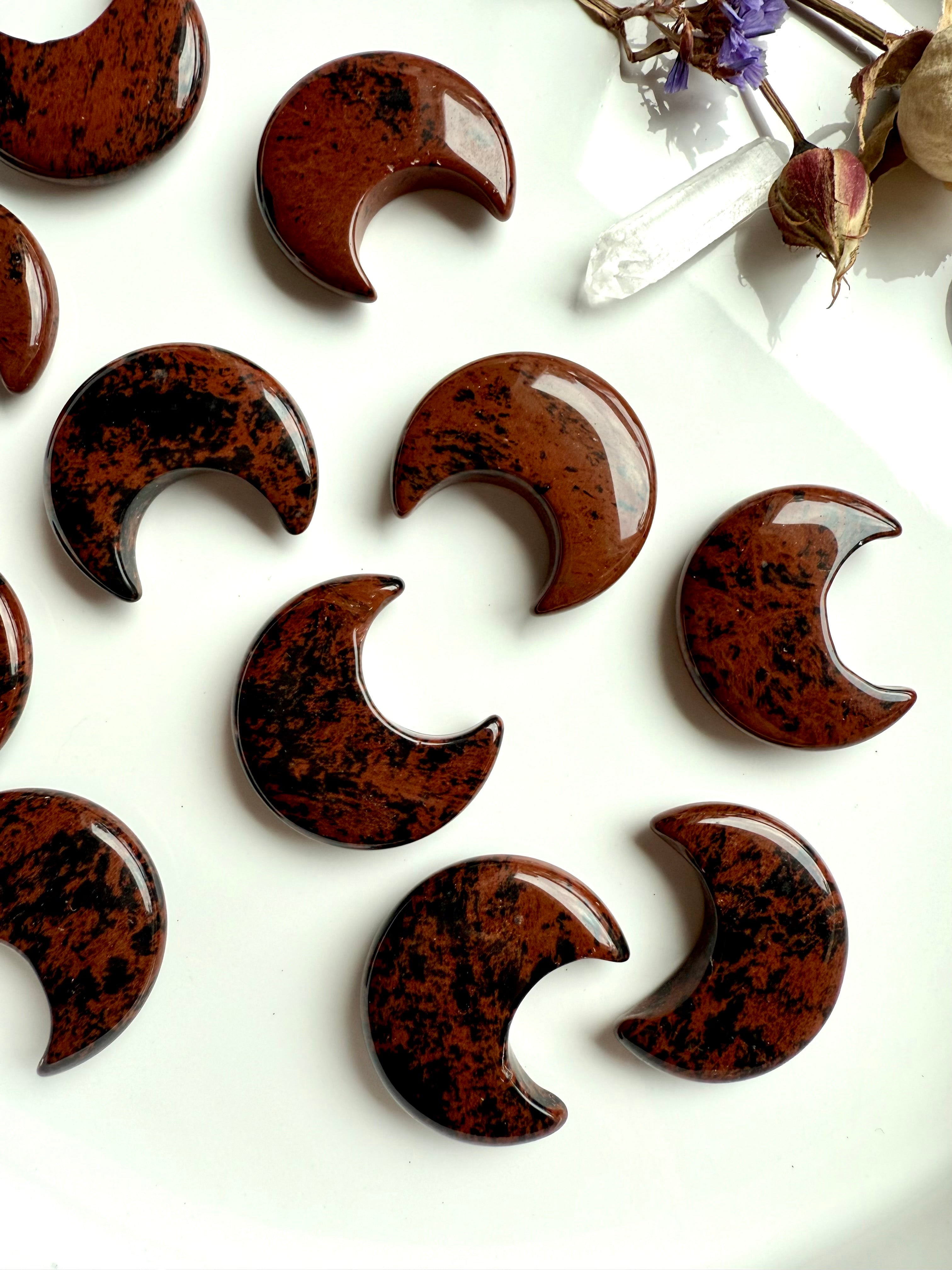 Detailed view of Mahogany Obsidian crescent moons on a white plate, showing unique black & red-brown patterns. Grounding stones for protection and stability.