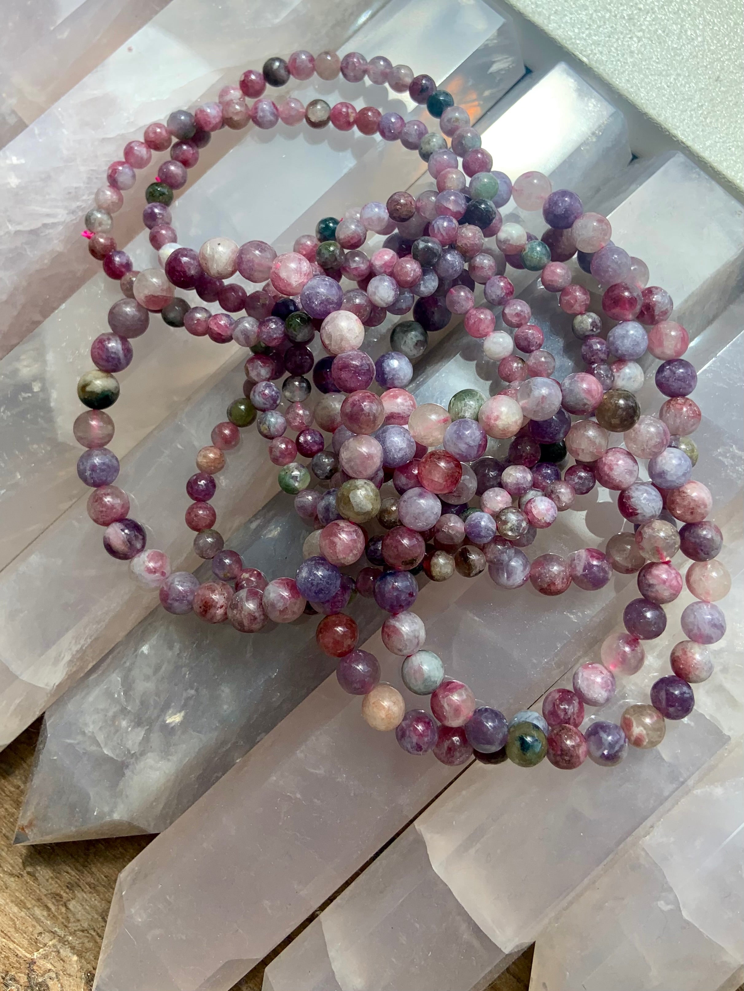 Overhead view of Green Unicorn Stone bracelets — Watermelon Tourmaline in Lepidolite — resting on crystal points. Heart chakra crystal jewelry for peace + emotional healing