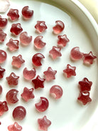 Polished Strawberry Quartz moon and star carvings in soft rose pink and vibrant red, showing variations in color and translucence 
