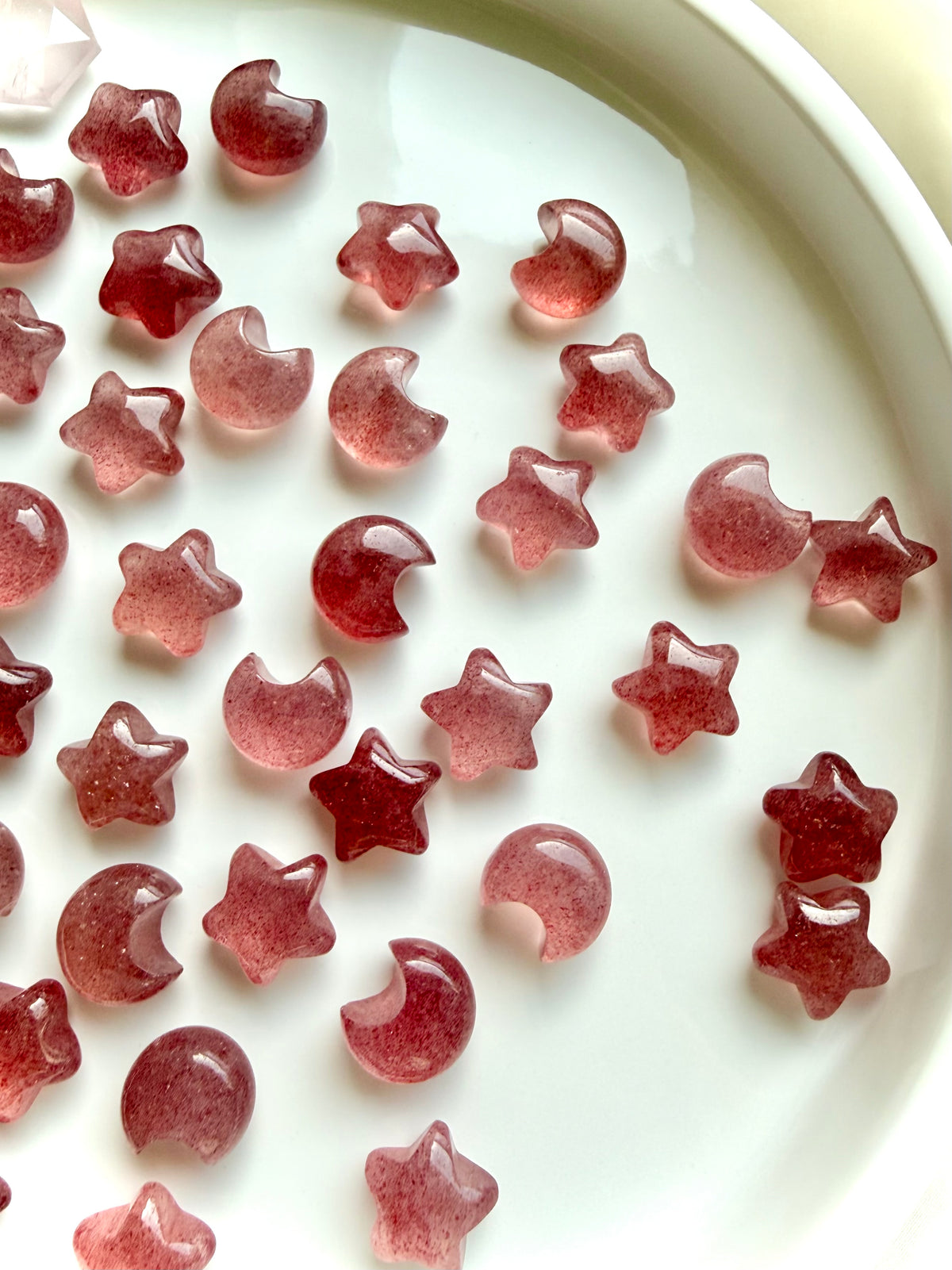 Polished Strawberry Quartz moon and star carvings in soft rose pink and vibrant red, showing variations in color and translucence 