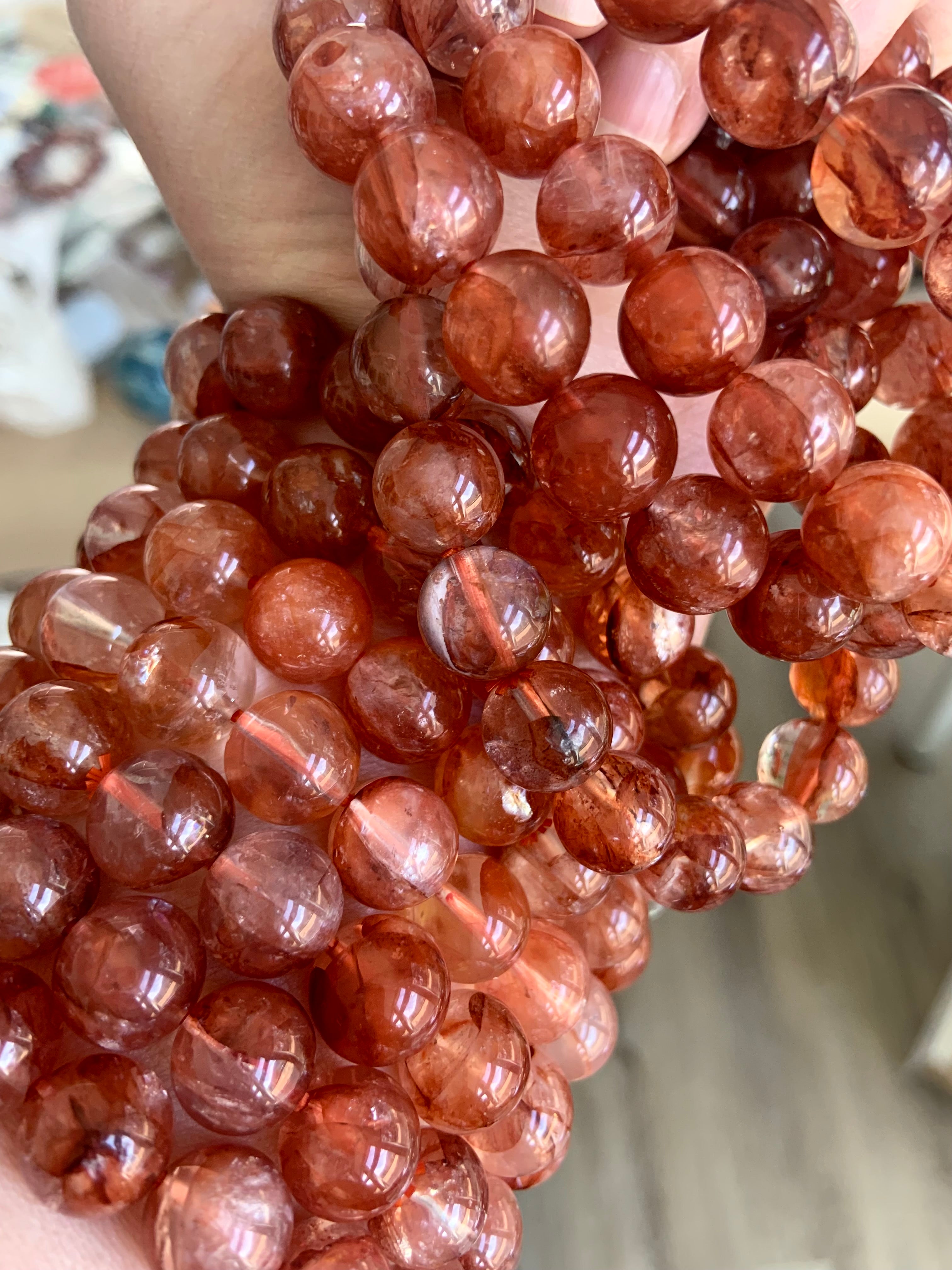 Stack of red Hematoid Quartz bracelets worn on wrist and held in hand, displaying variety and detail in the crystal beads