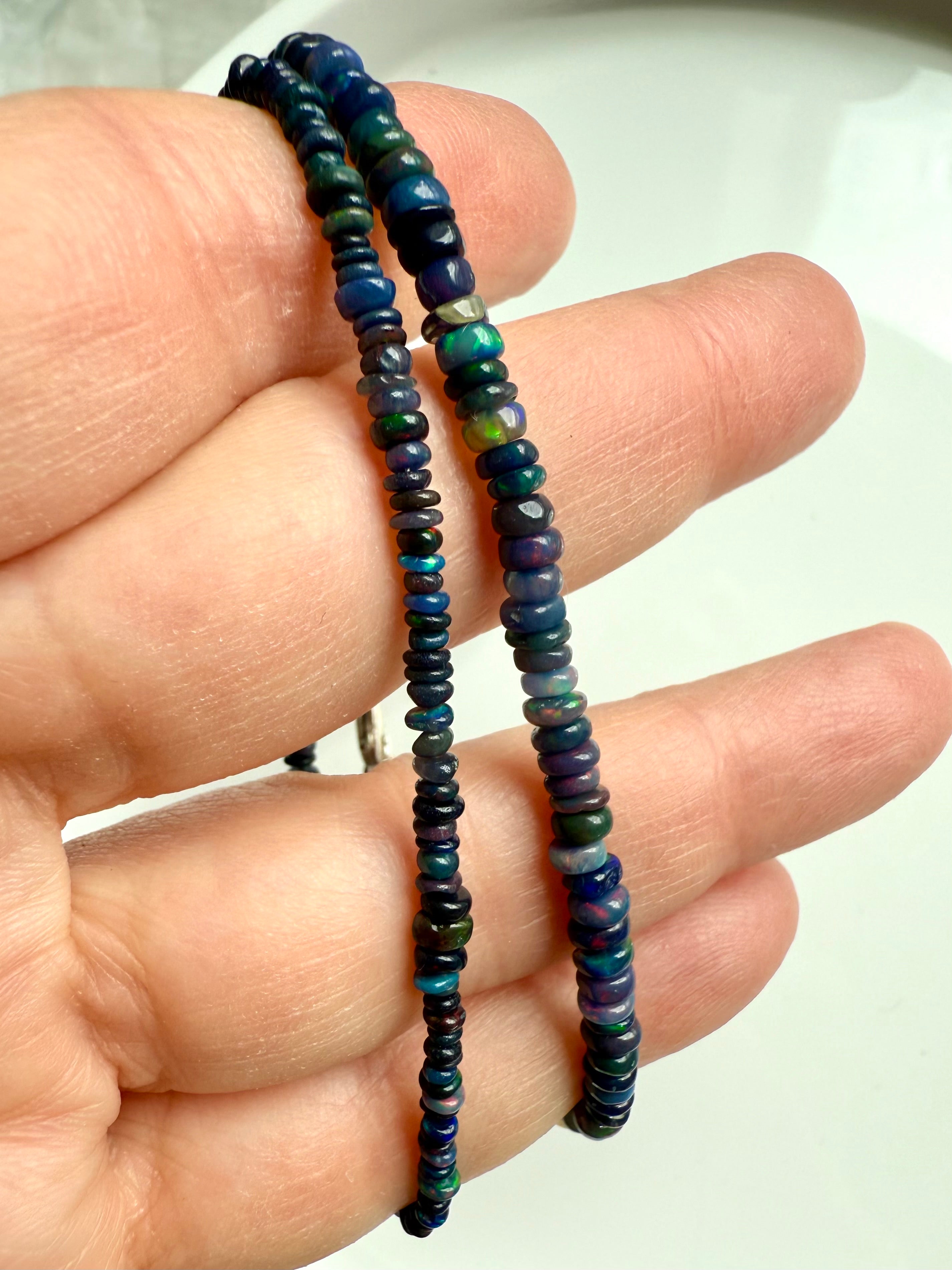 Close-up of two Black Fire Opal bracelets in different bead sizes — luminous Ethiopian opal beads with blue fire and rainbow sheen.