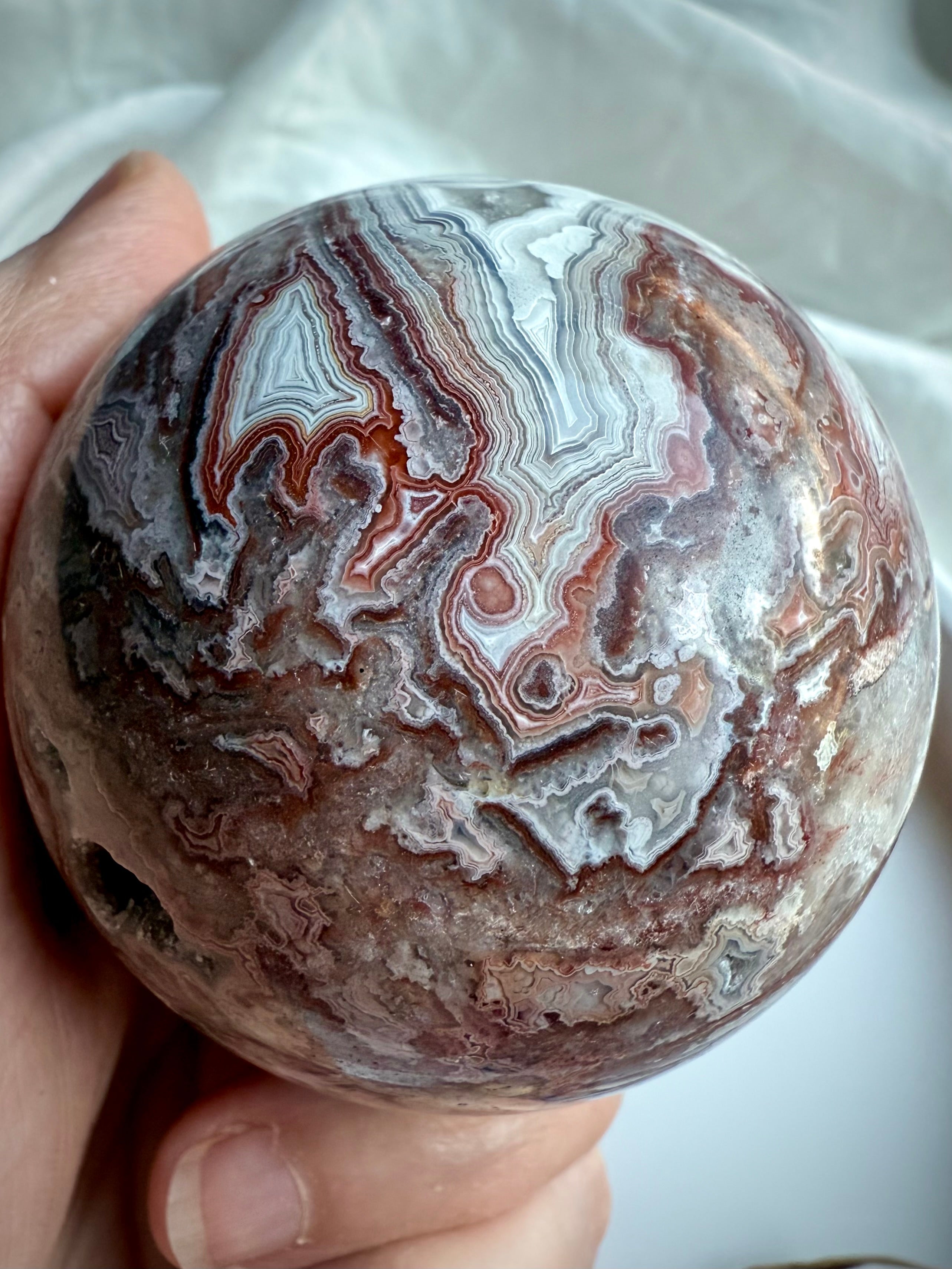 Closeup of Crazy Lace Agate sphere with bold red, white, and gray banding and root chakra 