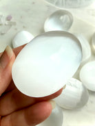 Polished Selenite palm stone resting in hand showing luminous satin spar sheen and comfortable meditation size