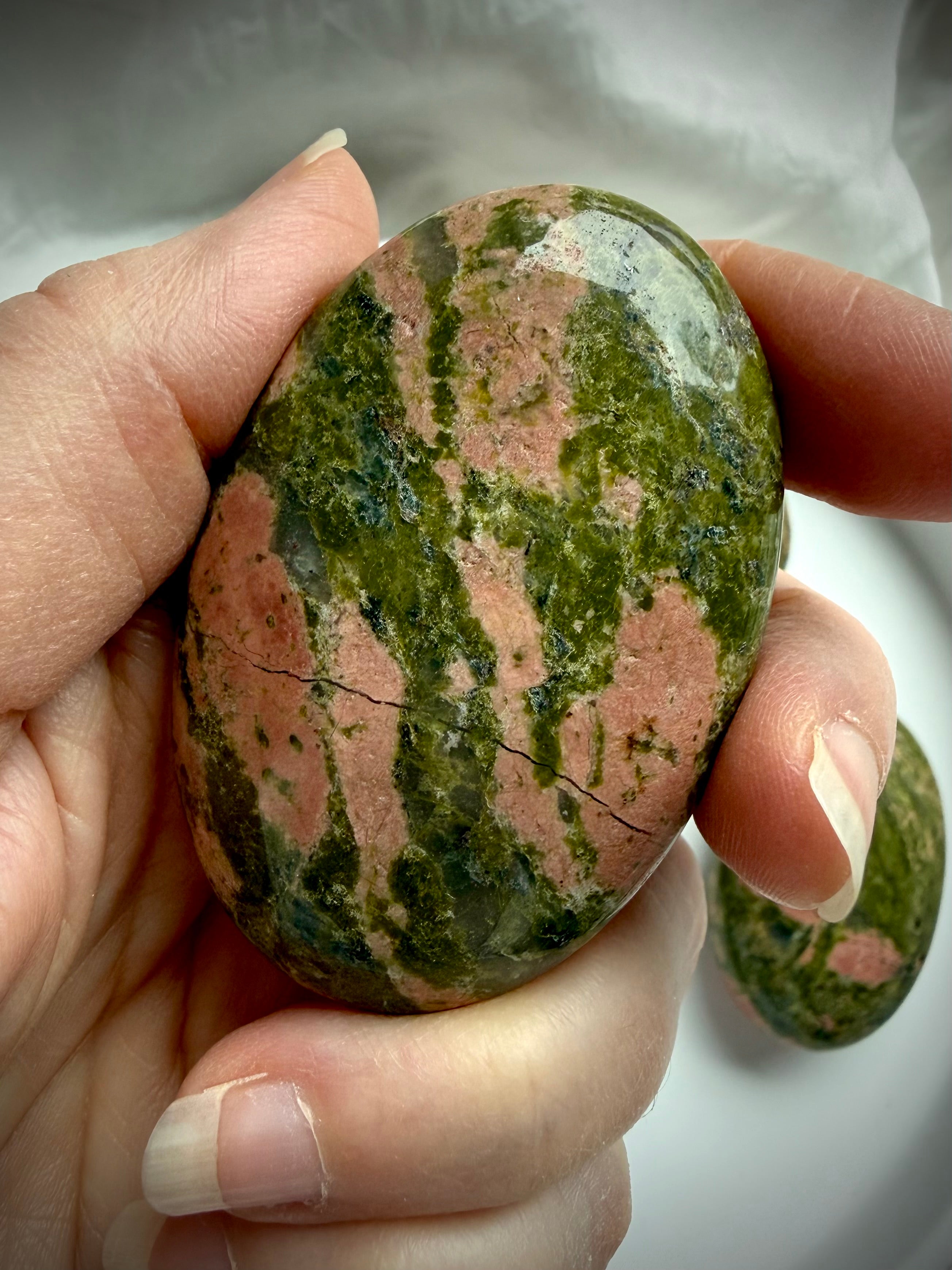 Unakite palm stone held in hand showing smooth polished surface with natural green epidote and pink feldspar