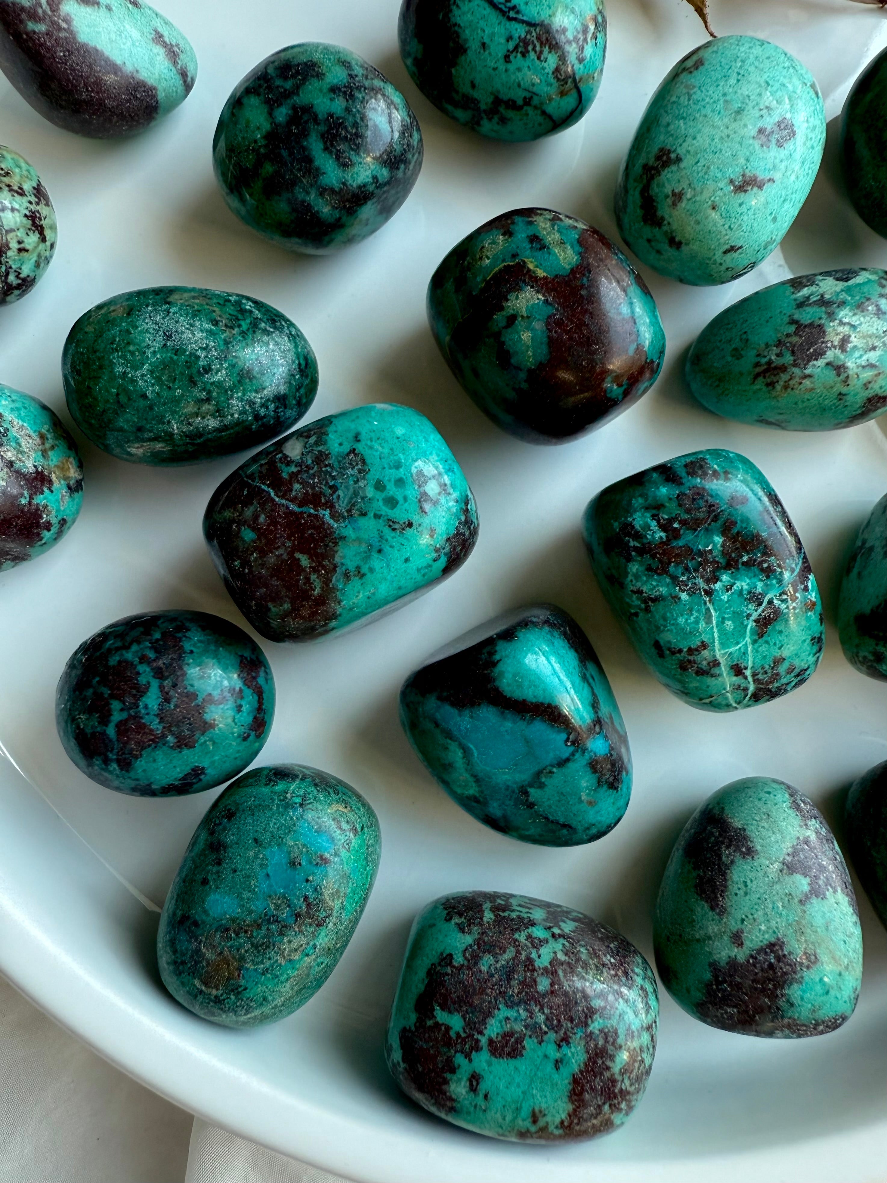 Detailed view of Chrysocolla tumble showing copper-rich turquoise-green hues with mottled red Cuprite and natural mineral texture.