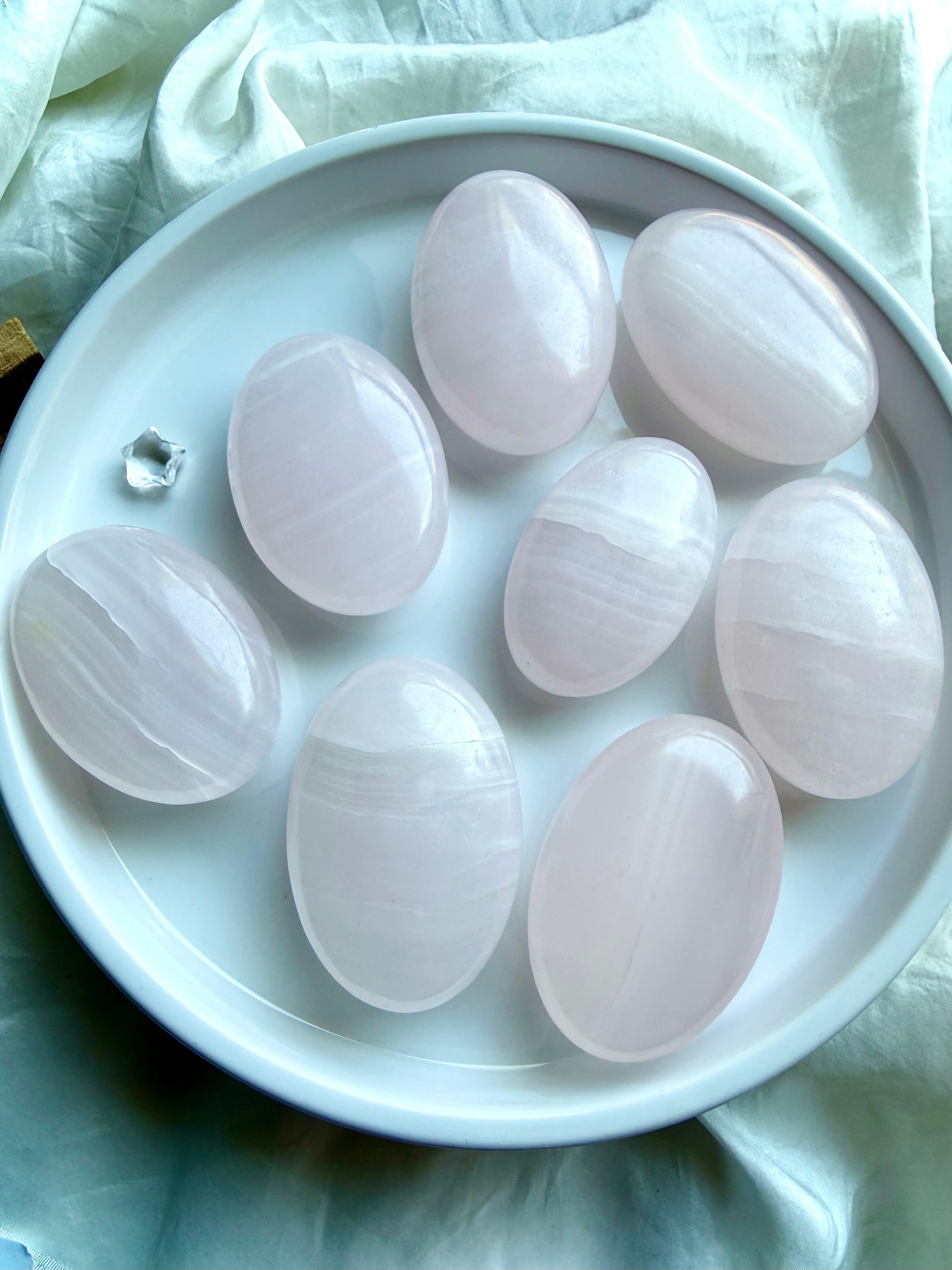 Mangano Calcite palm stones displayed on a white plate showing natural variation in pink color and banding