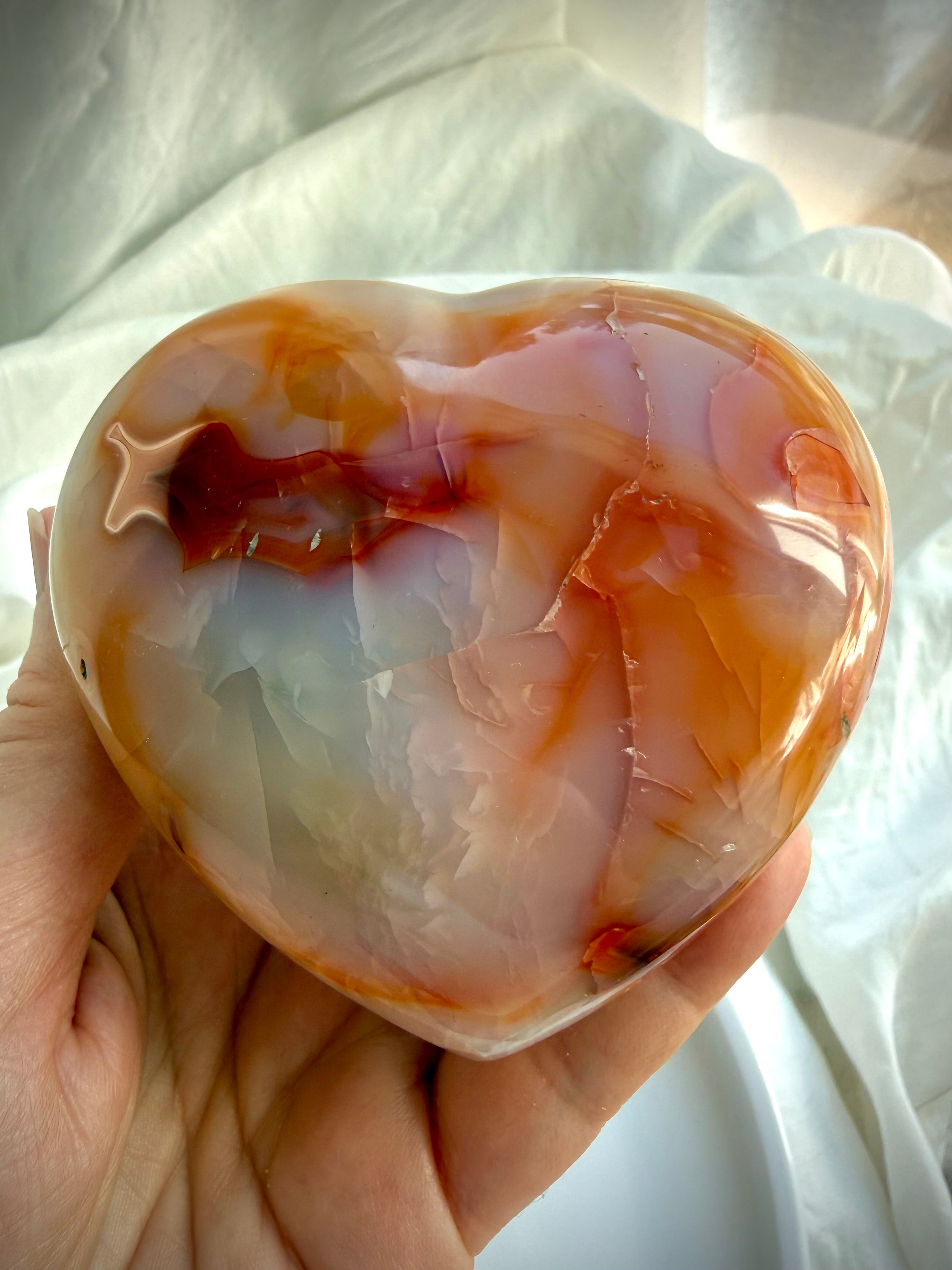Polished Carnelian heart crystal held in hand for size reference showing natural orange colors and smooth heart shape