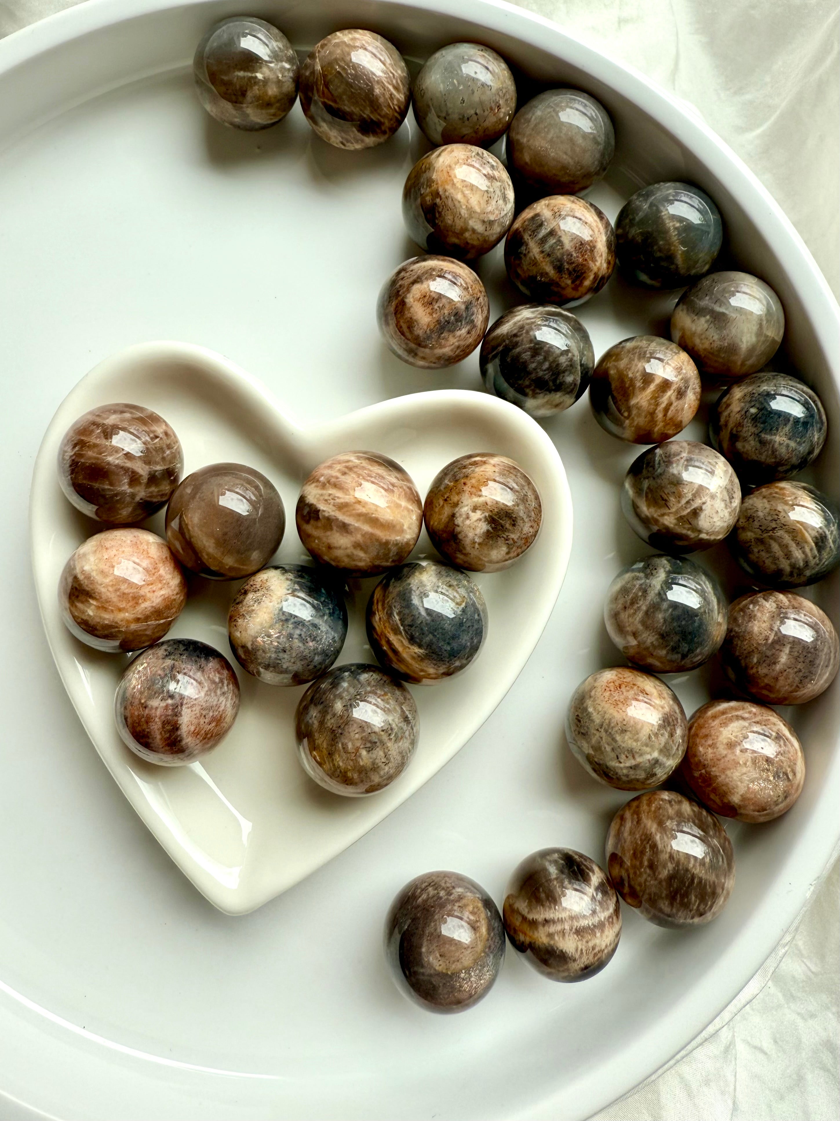 Grounding Mini Black Moonstone spheres with Sunstone shimmer in a white heart-shaped bowl for intuition