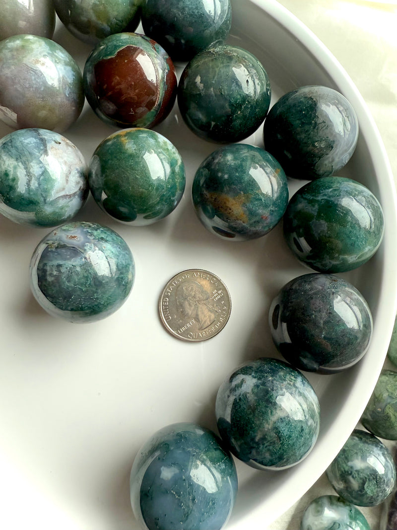 Colorful moss agate mini spheres shown on a white plate with a quarter for scale