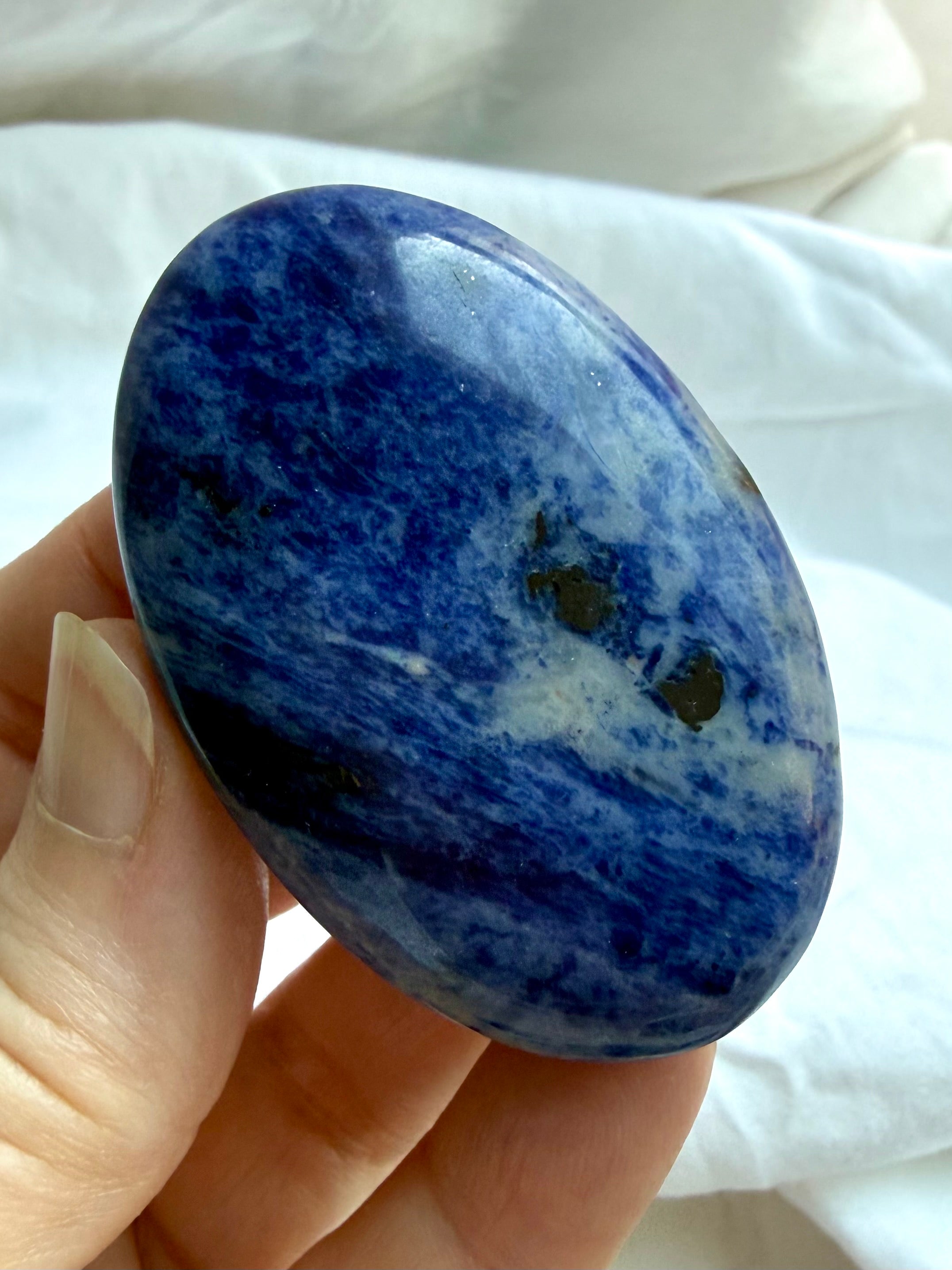 Sodalite palm stone held in hand with rich denim blue color and contrasting natural mineral patterns
