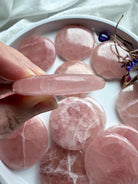 Side view of a Rose Calcite palm stone held between fingers, showing flat round shape, glossy polish, and thin shape for meditation use