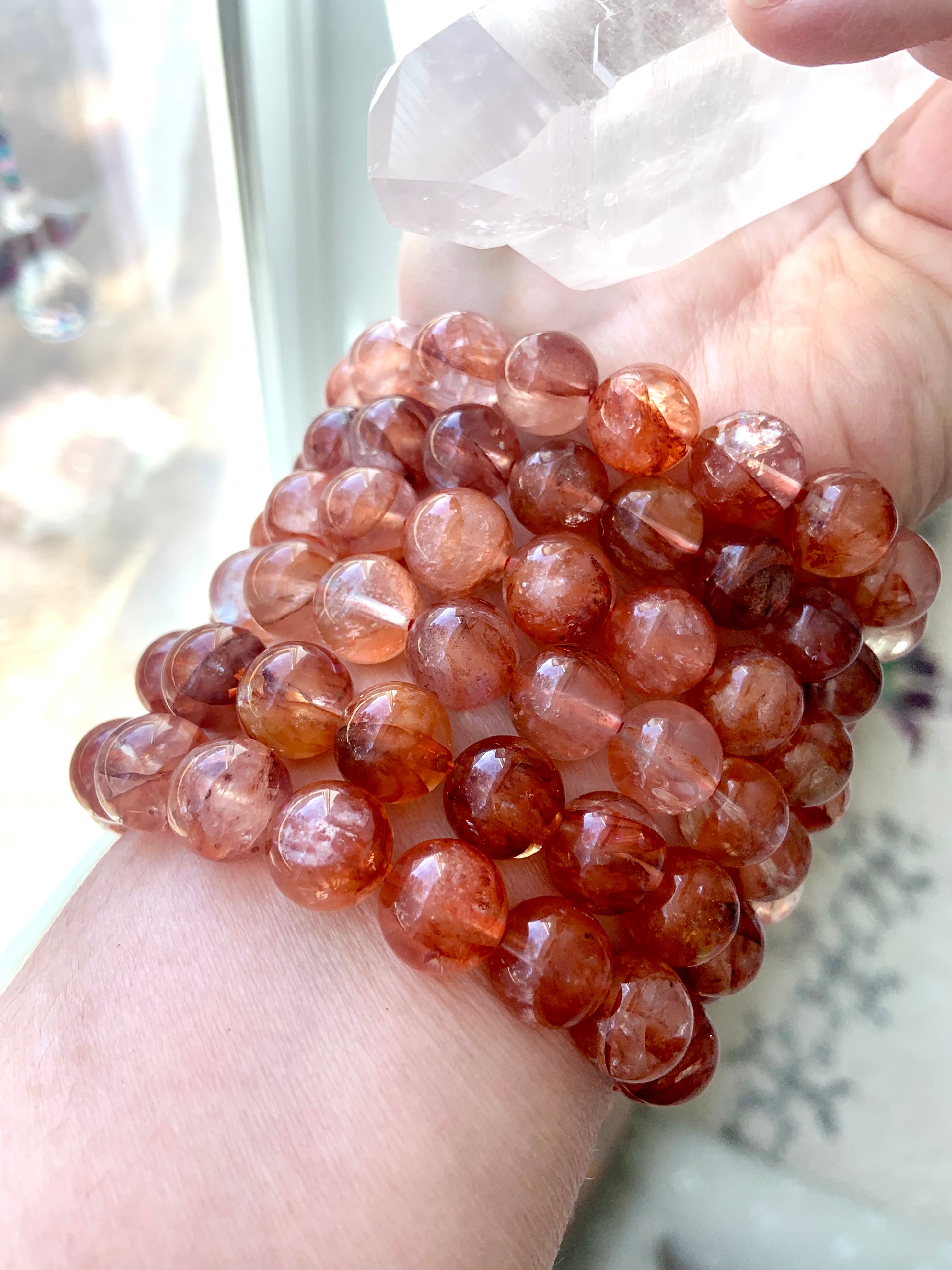 Stack of large Fire Quartz bracelets worn on wrist while holding a clear quartz crystal, showing vibrant energy and bold 11.2–11.8mm beads