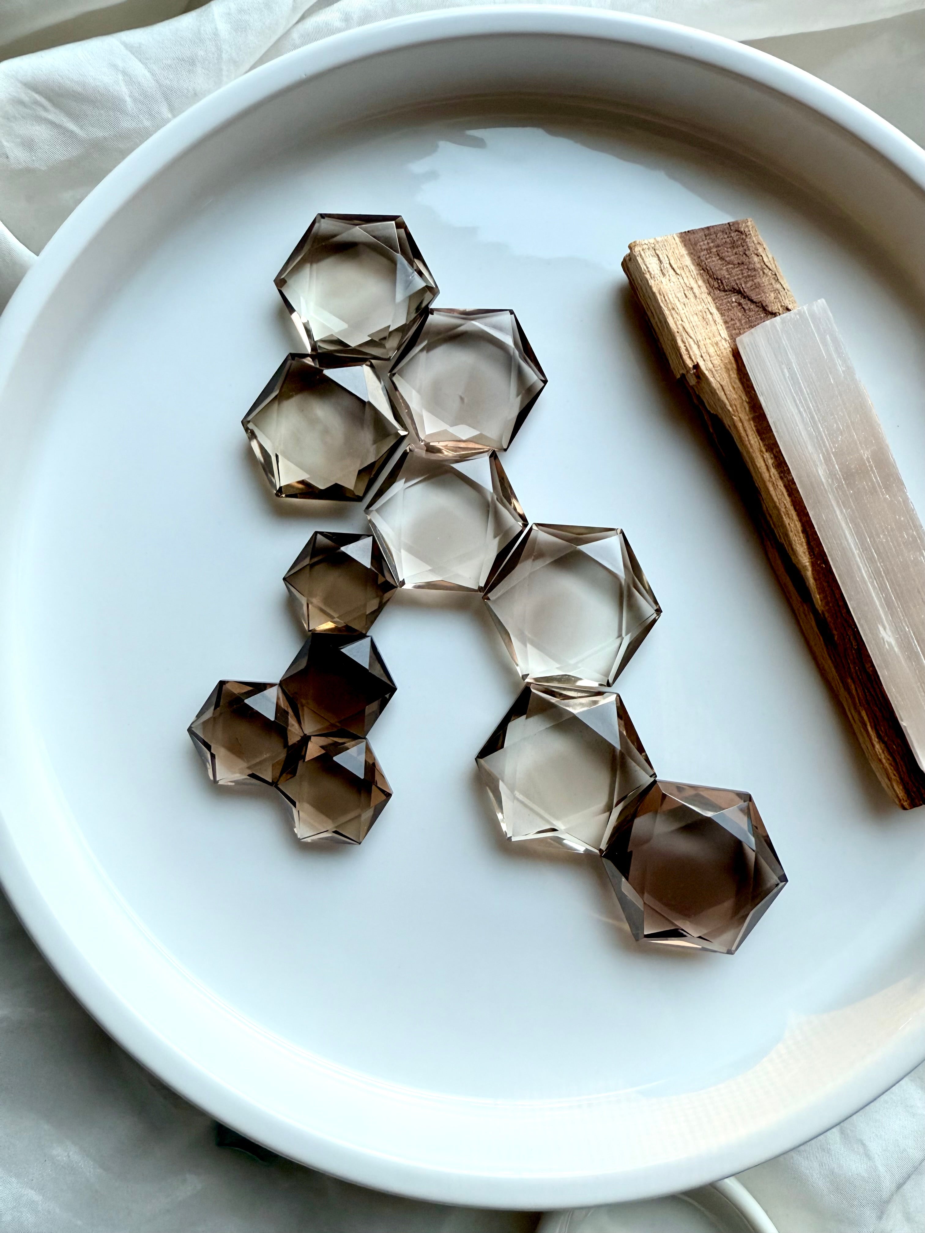Collection of faceted smoky quartz gemstones on a white tray with palo santo and selenite – Root Chakra crystals for grounding and energy work.