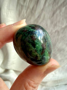 Natural Ruby in Zoisite tumbled stone held between fingers, showing rich emerald green, dark mineral inclusions and ruby pink coloring