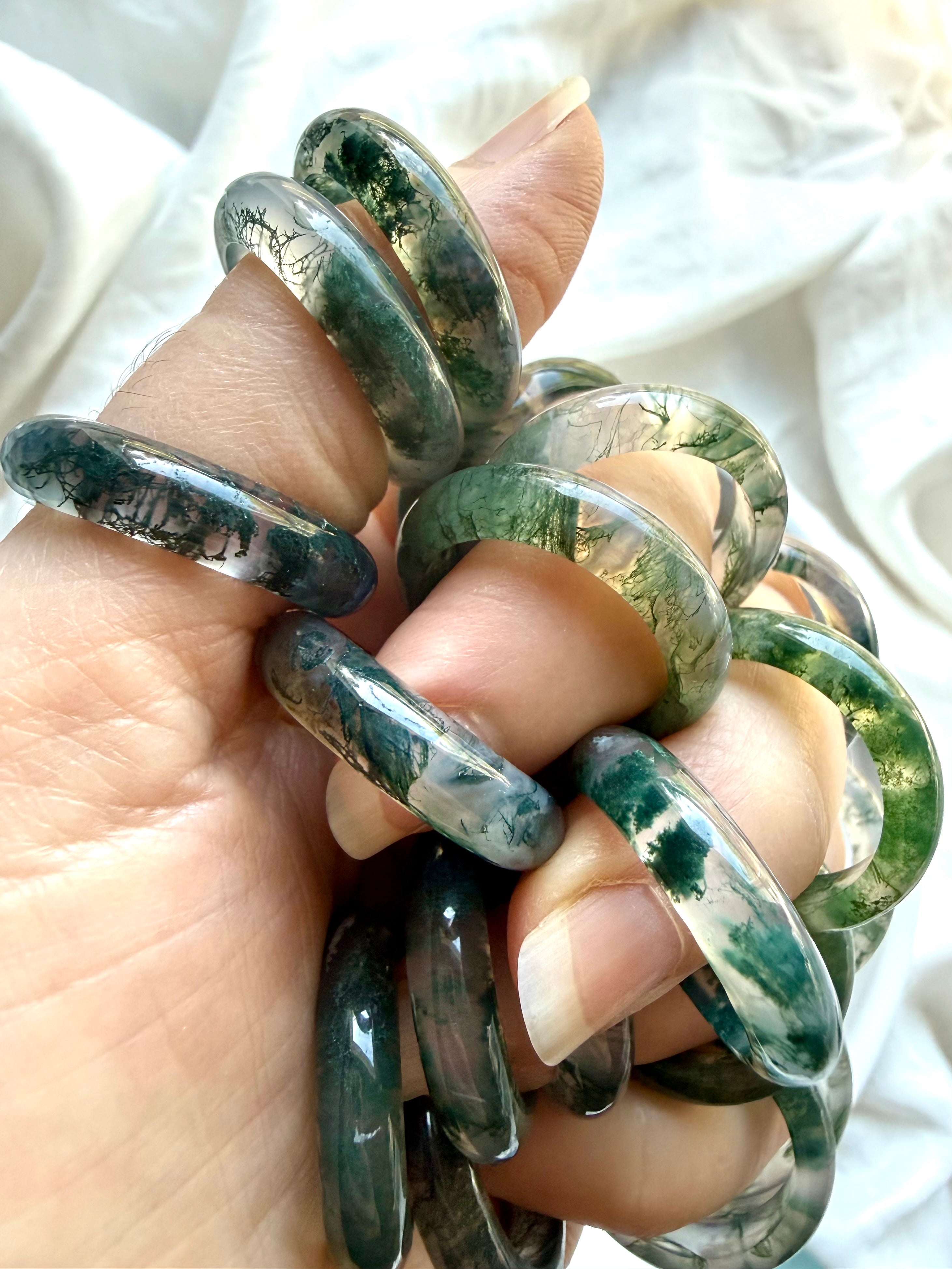 hand holding moss agate band rings showing natural inclusions and polished finish, translucent crystal ring for calm balance and renewal