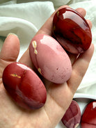 large polished Mookaite Jasper palm stone held in hand with rich earthy tones for grounding and confidence