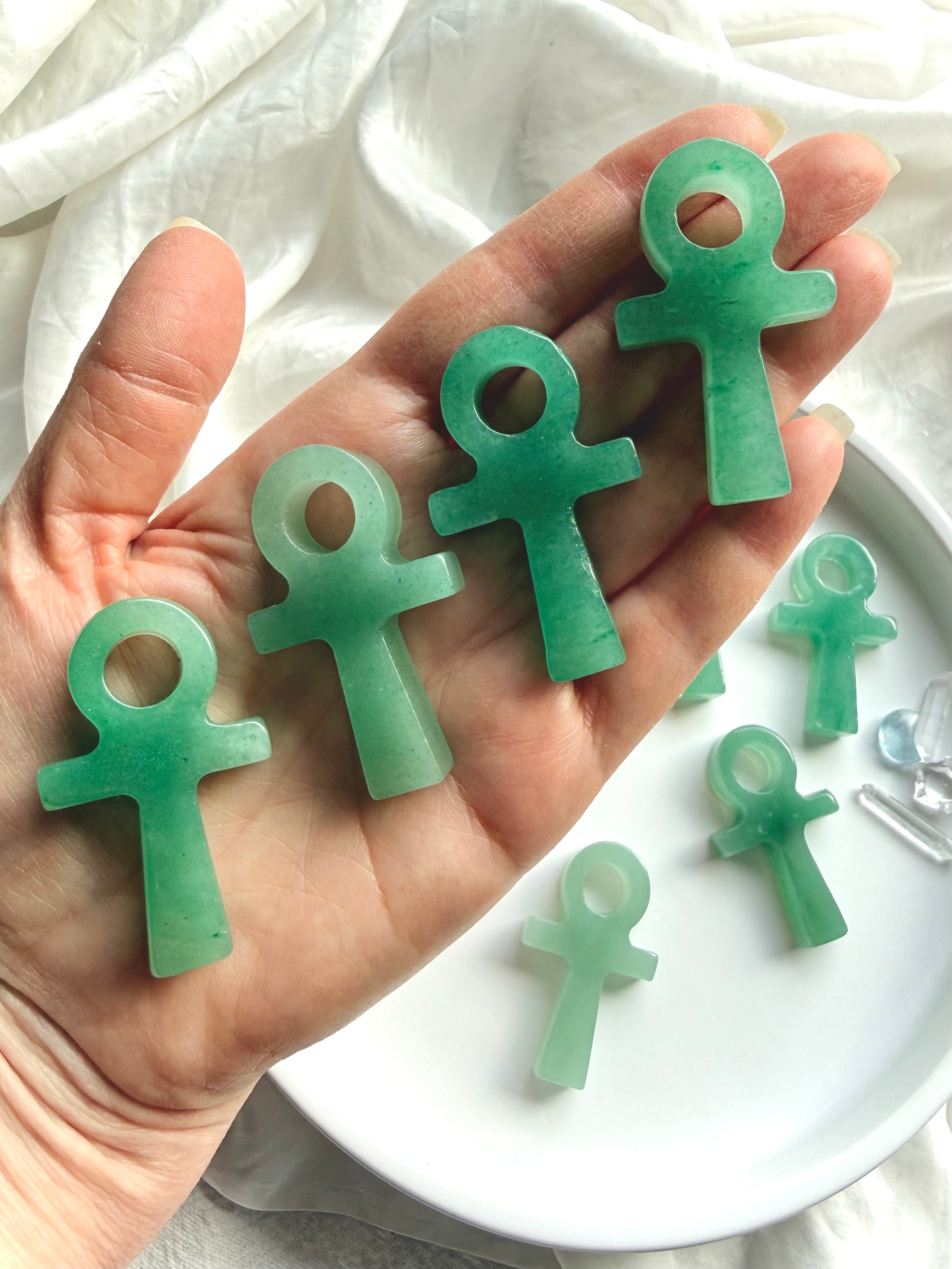 Polished green aventurine ankh carvings with soft translucent green tones shown on hand for scale