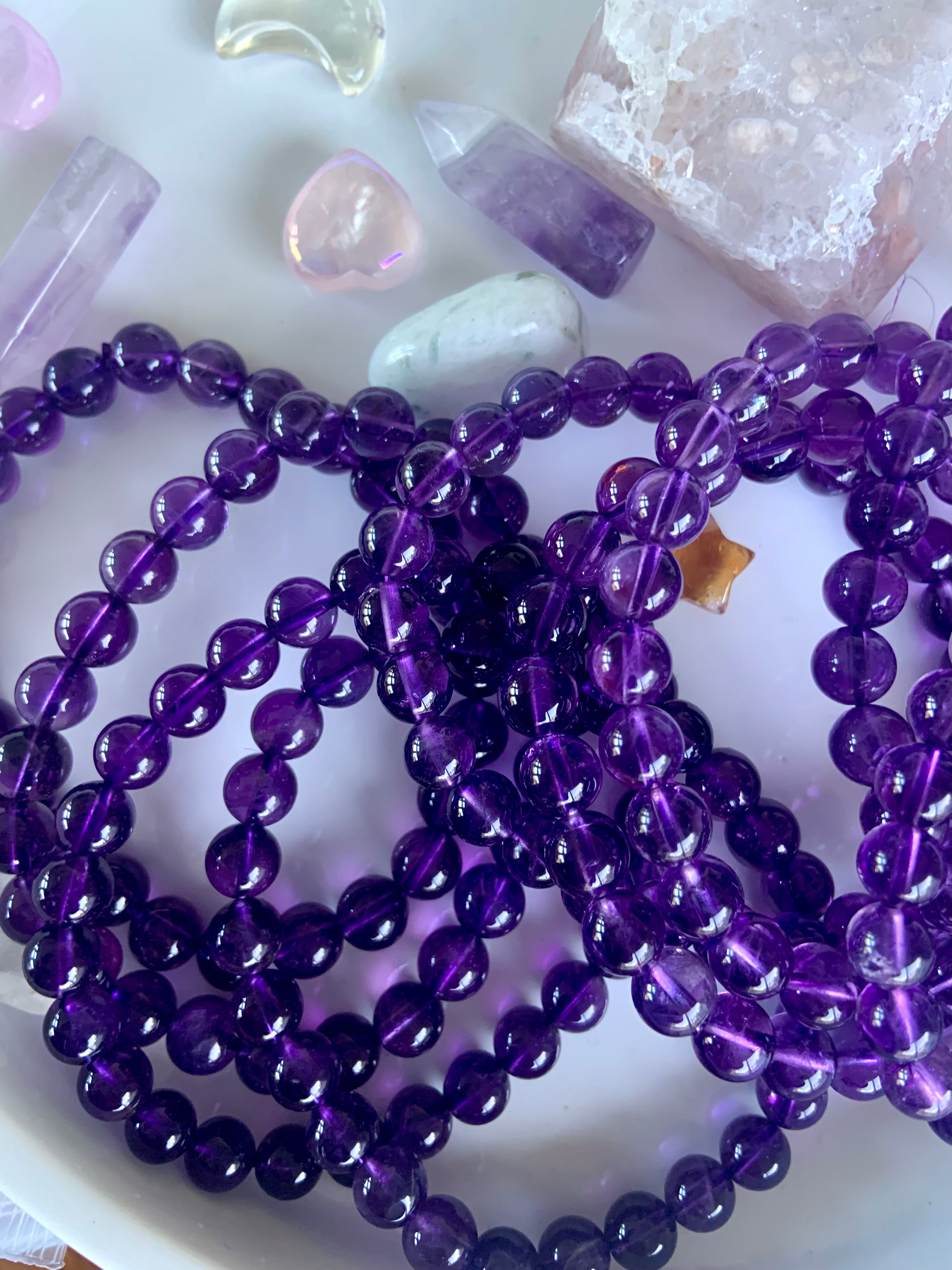 Overhead view of deep purple amethyst crystal bead bracelets on a white plate with mini crystals in the background